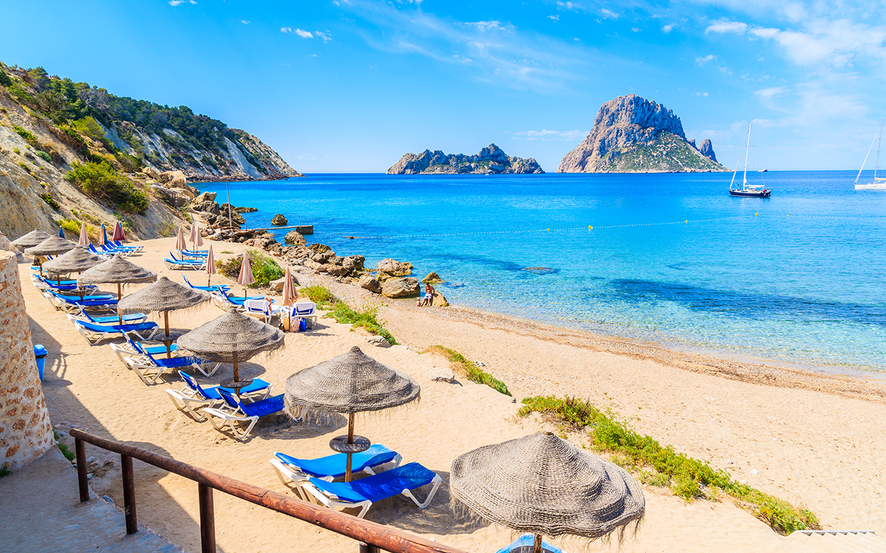 View of Cala d'Hort beach with sunbeds and umbrellas and beautiful azure blue sea water, Ibiza island, Spain
