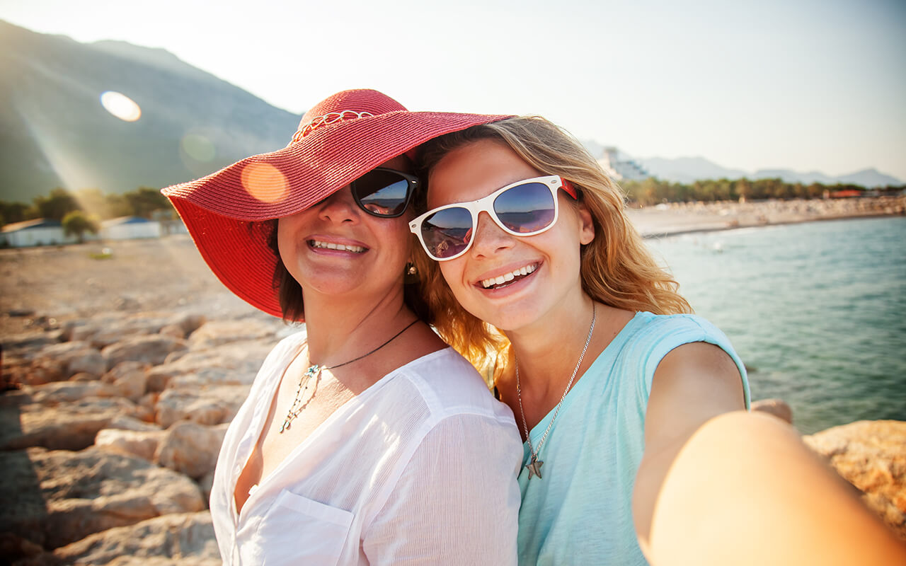 An attractive middle-aged woman with her adult daughter doing selfie on the beach, vacation and travel, cruise and sea