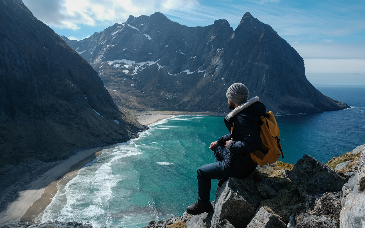 Man sitting on cliff edge alone enjoying aerial view backpacking lifestyle travel adventure outdoor vacations in Norway top of Reinebringen mountain.