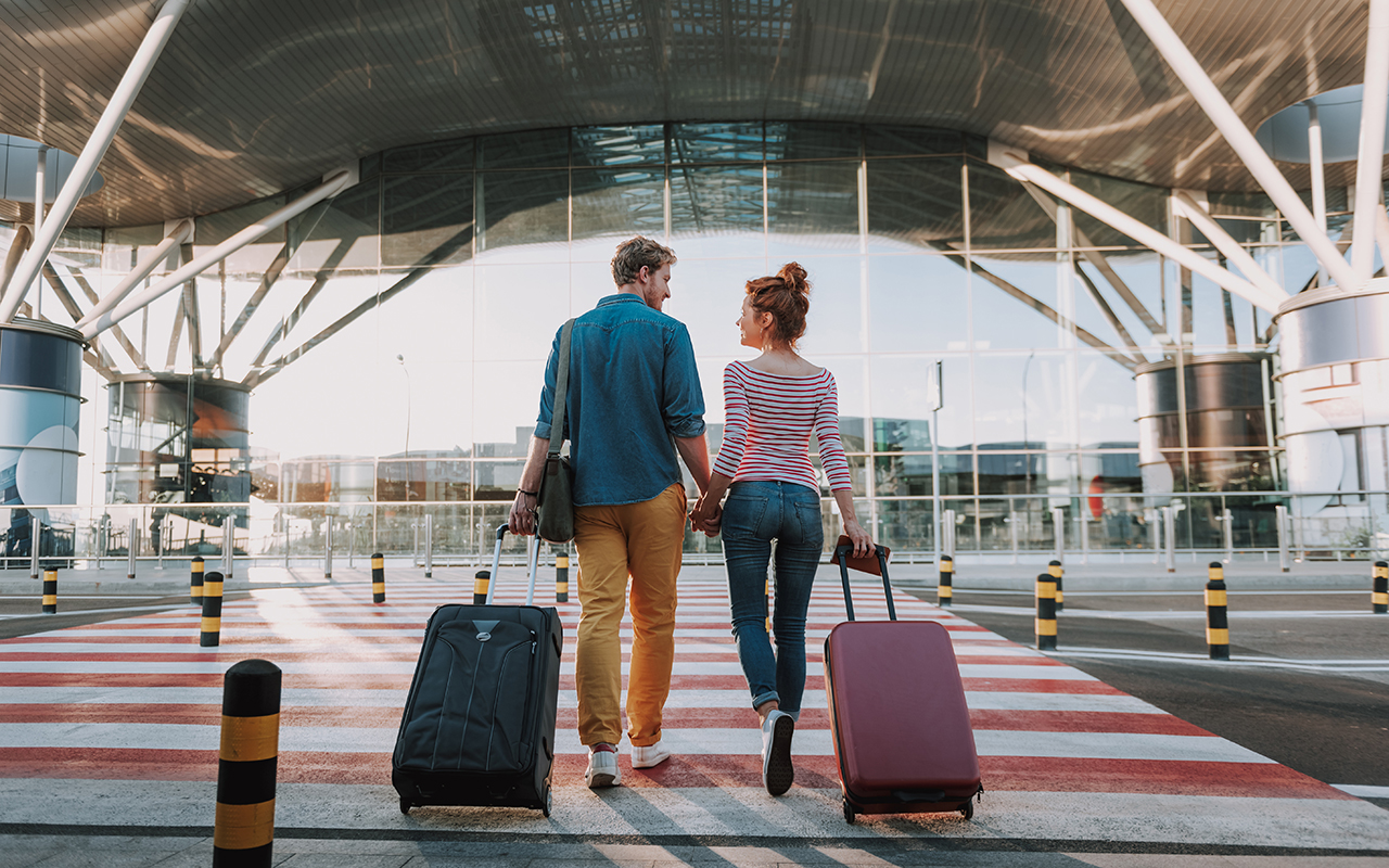 Beautiful loving couple with travel suitcases holding hands in airport
