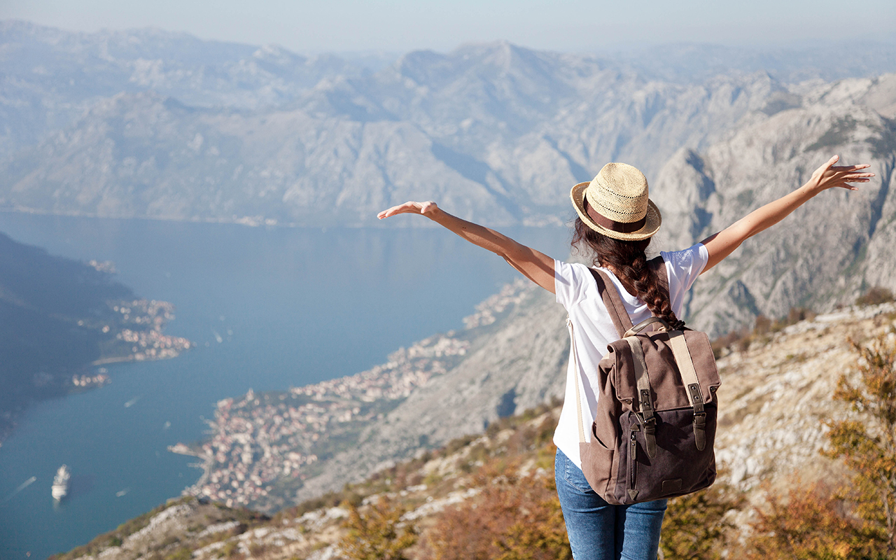 Traveler with backpack on mountain top. Happy woman with raised arms in amazing landscape.
