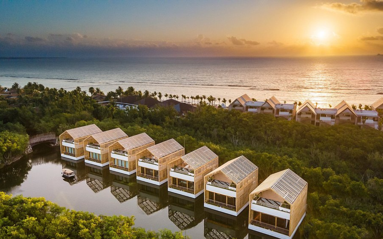 Scenic view of the Banyan Tree Mayakoba Hotel in Playa del Carmen, featuring lush tropical greenery, serene canals, and luxury villas with thatched roofs nestled in the mangroves.