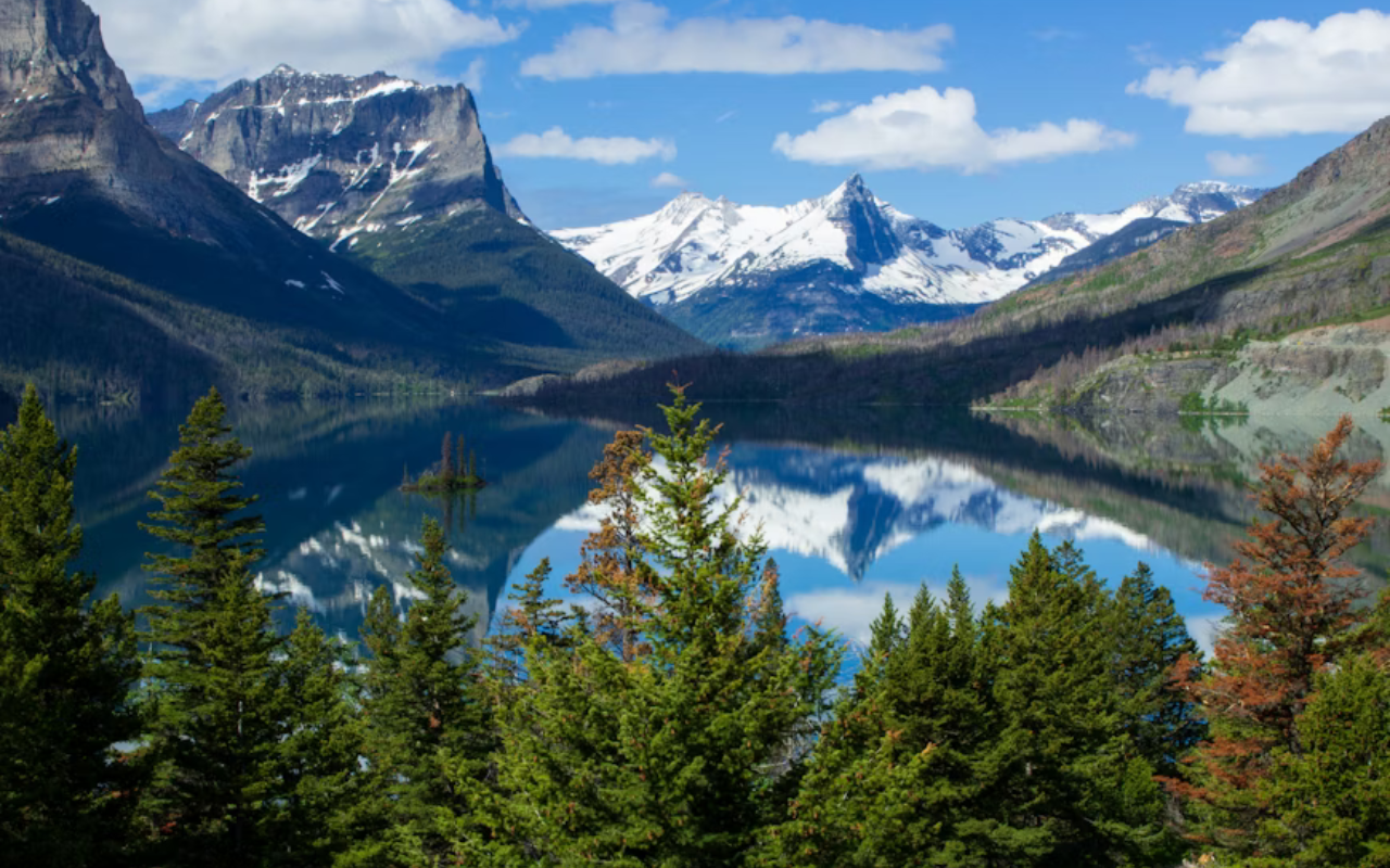 Snow-capped mountains surround a expansive lake in Glacier National Park.