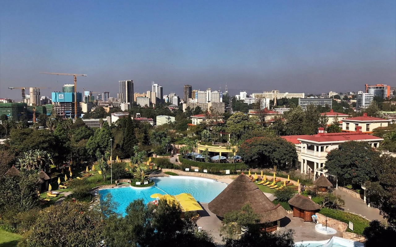 Cityscape of Addis Ababa, Ethiopia with modern high-rises, construction cranes, and a resort pool surrounded by tropical greenery