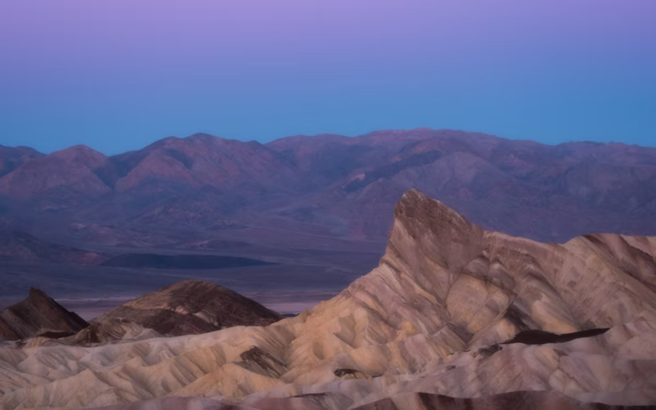 The sun sets over the dry desert terrain of Death Valley National Park.