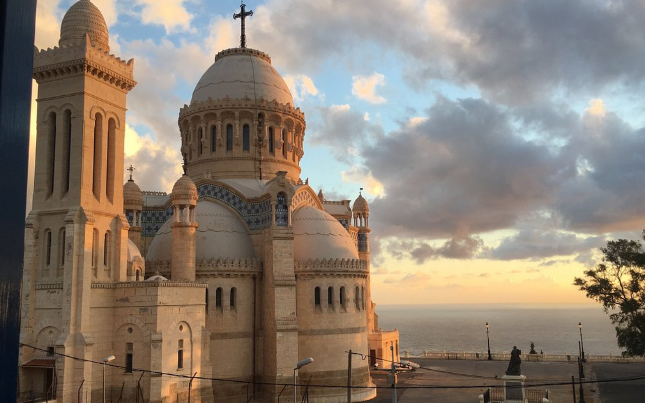 Historic Roman Catholic basilica Notre-Dame d’Afrique in Algiers, Algeria, glowing in the sunset with views of the Mediterranean coastline