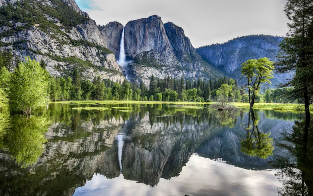 A waterfall pours from steep granite cliffs into a calm lake surrounded by lush green trees.