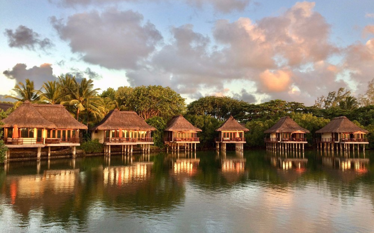 Constance Prince Maurice Hotel in Mauritius, showcasing overwater villas on stilts above a calm turquoise lagoon, surrounded by lush palm trees and tropical foliage.