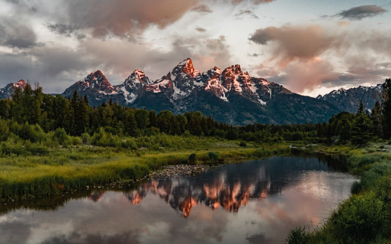 The sun sets on Grand Teton National Park, giving the lake and mountain peaks warm orange glow.