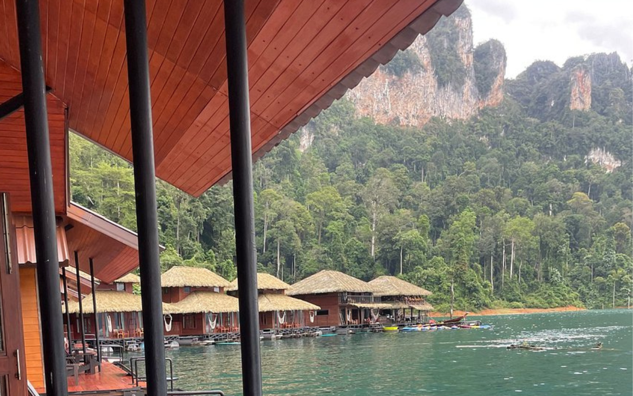 Floating bungalows of Panvaree Resort nestled on a calm emerald lake, surrounded by towering limestone cliffs and lush rainforest in Khao Sok National Park, Thailand.