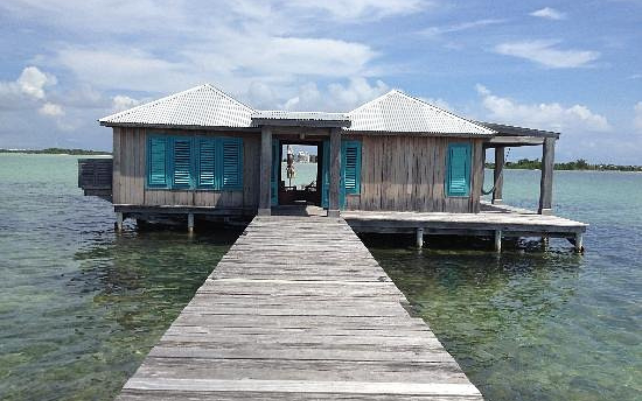 Secluded overwater villa at Cayo Espanto Hotel in Belize, perched above the turquoise Caribbean Sea with a private dock. Surrounded by crystal-clear water, the luxurious retreat offers an intimate island escape in a lush tropical paradise.