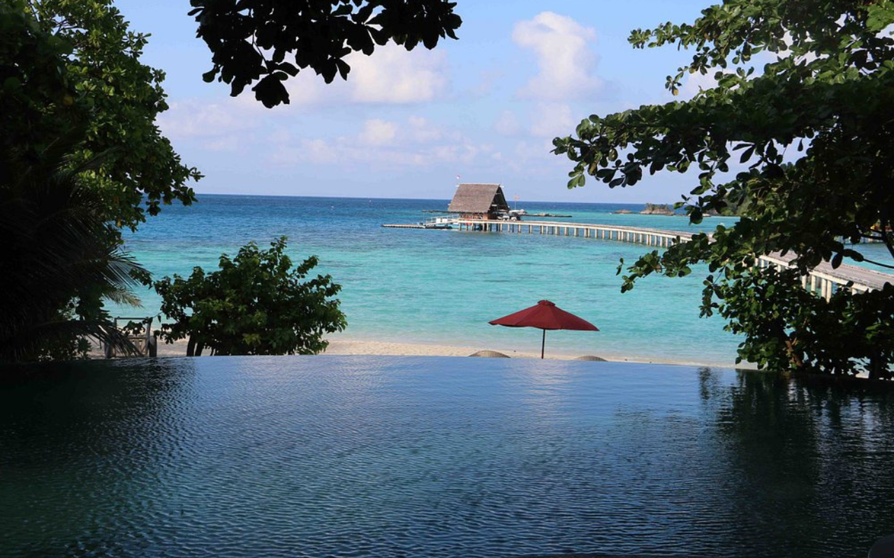 Luxury overwater and beachfront villas at Bawah Reserve Hotel in Indonesia, surrounded by crystal-clear lagoons, coral reefs, and lush jungle-covered islets. The serene eco-resort blends seamlessly with the natural seascape, offering an exclusive escape in the remote Anambas Archipelago.