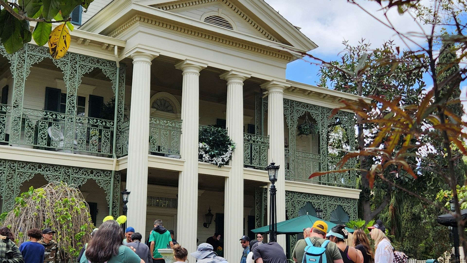 Disney’s Haunted Mansion attraction, showcasing its stately brick façade, wrought-iron balconies, and gothic architecture surrounded by eerie landscaping.