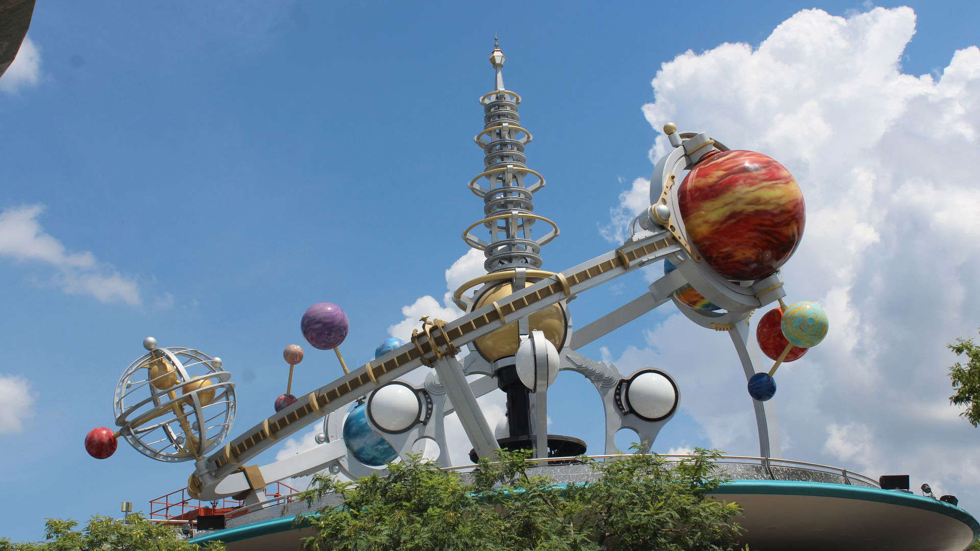 Disney’s Astro Orbiter ride, circling high above Tomorrowland on a towering platform with a golden planetary sculpture at its center.