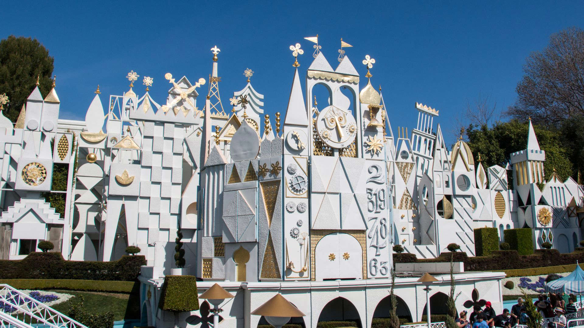 Whimsical white and gold façade of Disney’s It’s a Small World attraction, featuring geometric shapes, spinning clock elements, and stylized global architecture.
