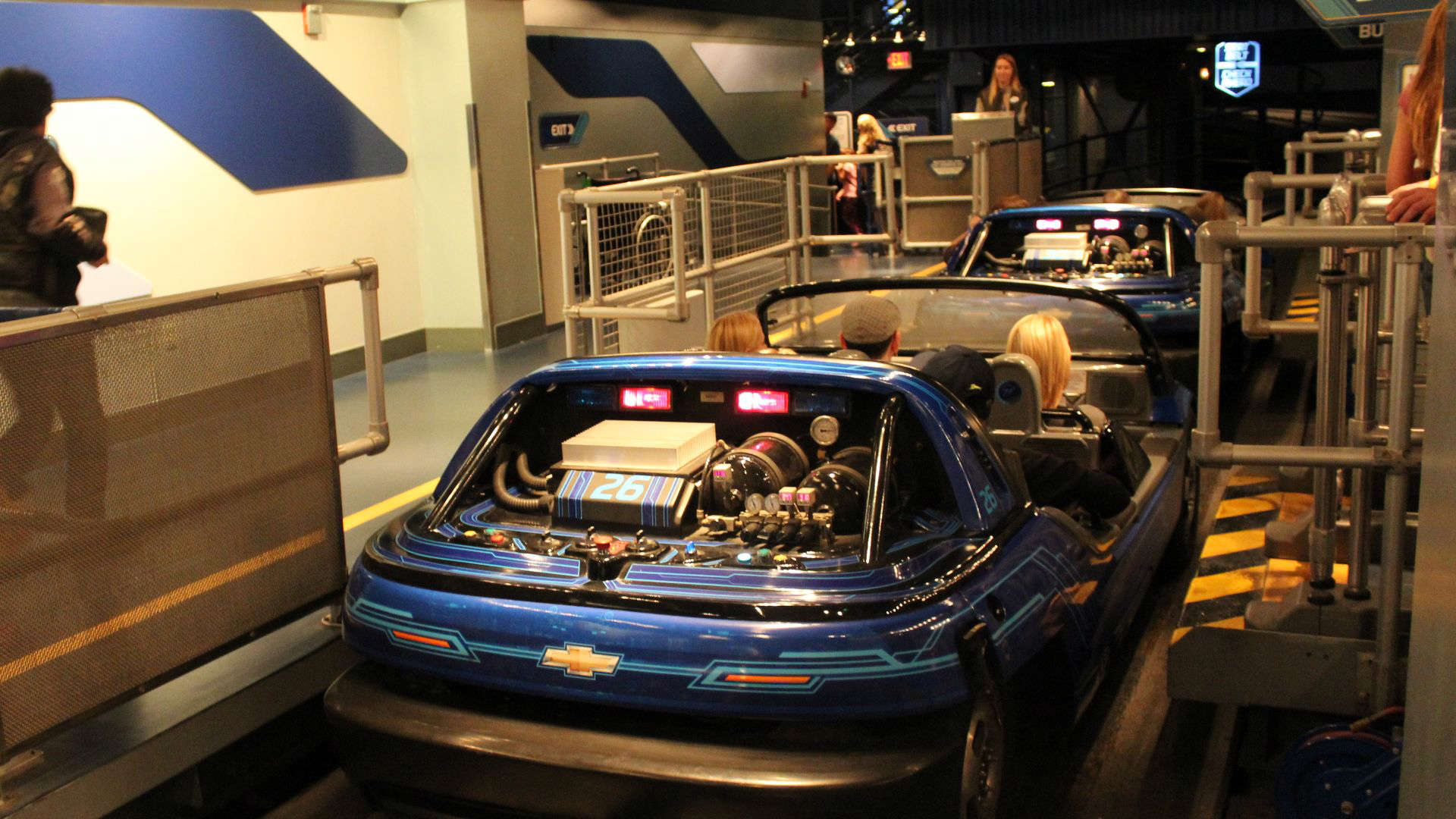 Guests loading into futuristic, open-air ride vehicles at Disney’s Test Track attraction, surrounded by a sleek, industrial-themed loading bay.