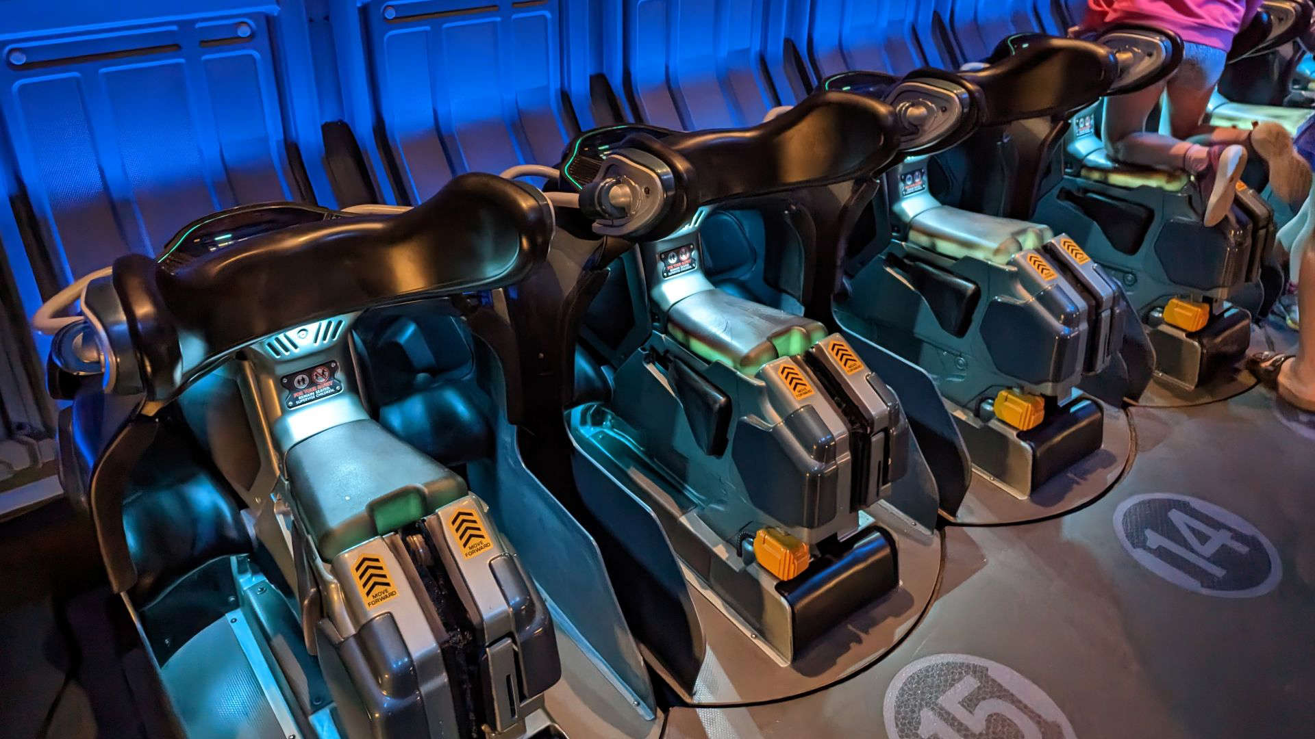 Ride vehicles resembling futuristic bikes lined up inside the Avatar Flight of Passage attraction at Disney’s Animal Kingdom. Set in a dimly lit, high-tech lab environment, the seats are designed to simulate flying on a banshee, enhancing the immersive experience on the planet of Pandora.