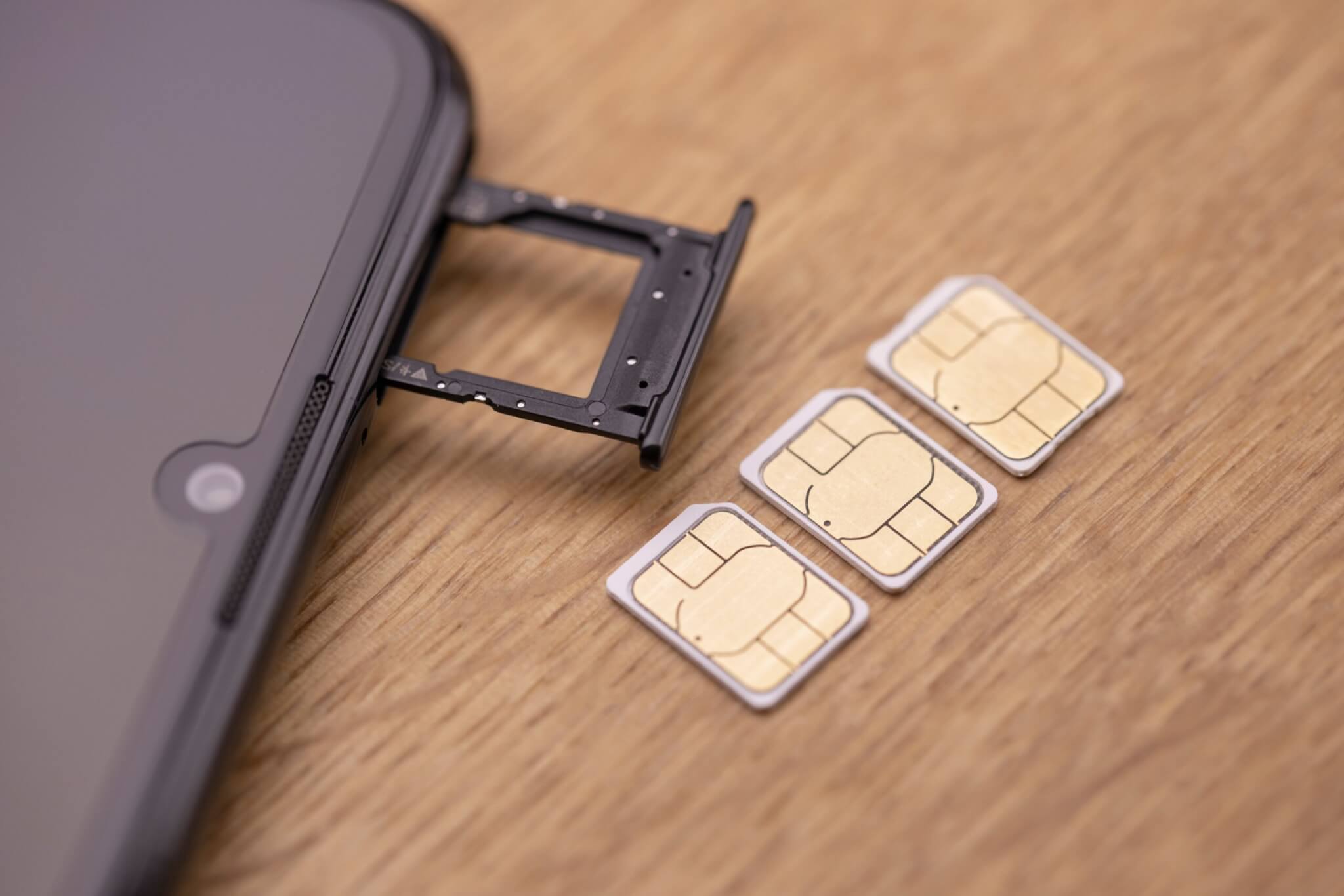 Cell phone with an open SIM card slot and three separate SIM cards laying on a wooden table.