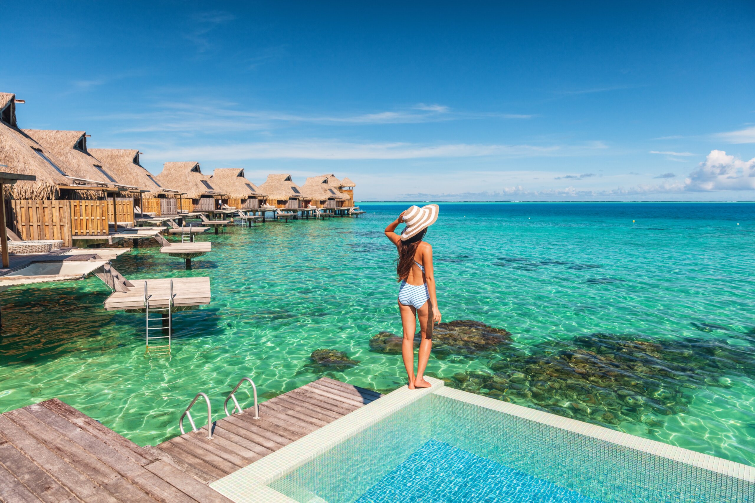 Travel luxury resort woman overwater bungalow hotel in Maldives. Luxury vacation hotel in Tahiti woman relaxing at infinity pool in French Polynesia.