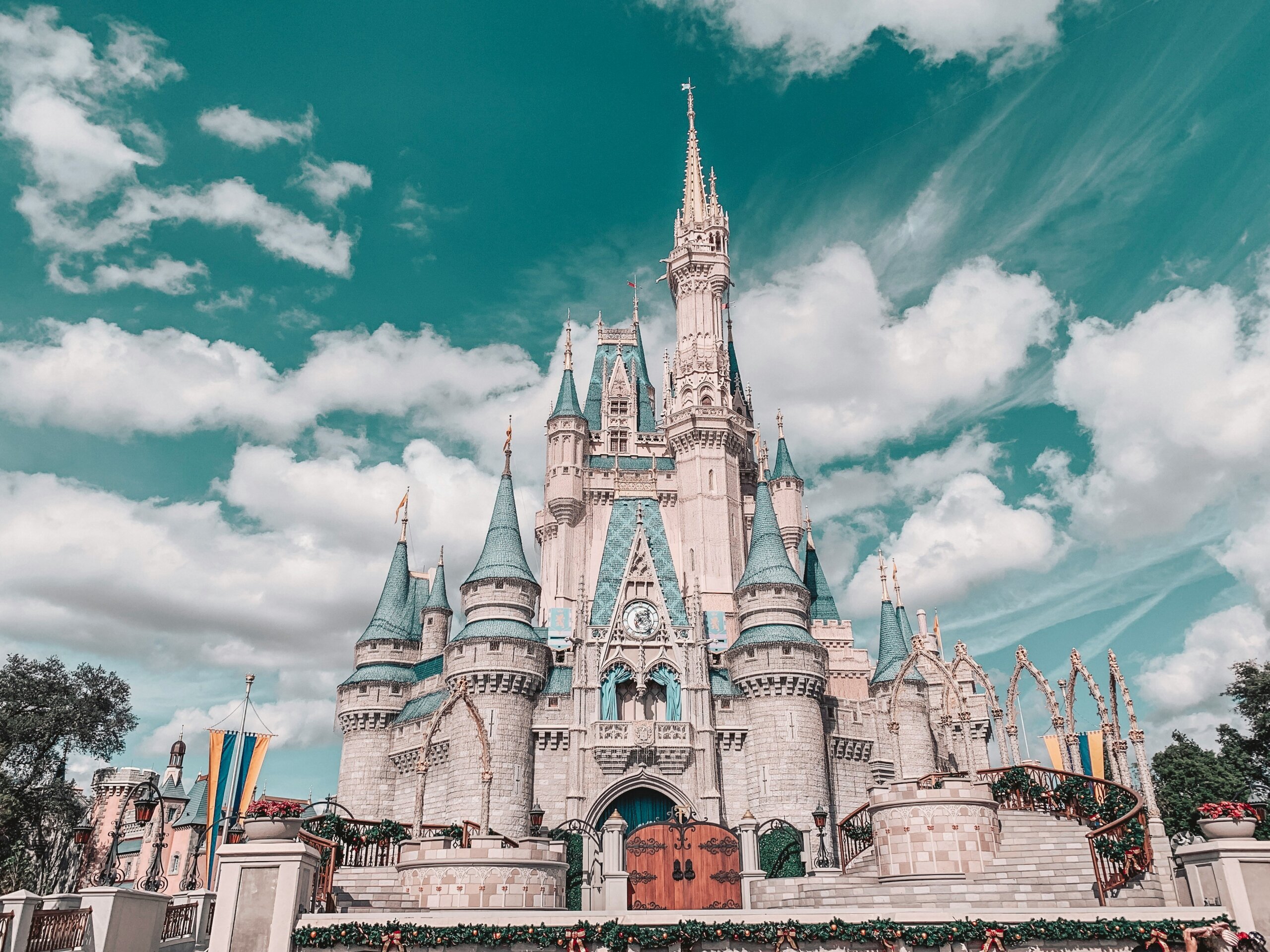 Front view of Cinderella Castle at Walt Disney World in Orlando, Florida, with its iconic blue turrets, detailed stonework, and festive decorations under a bright turquoise sky with fluffy clouds.