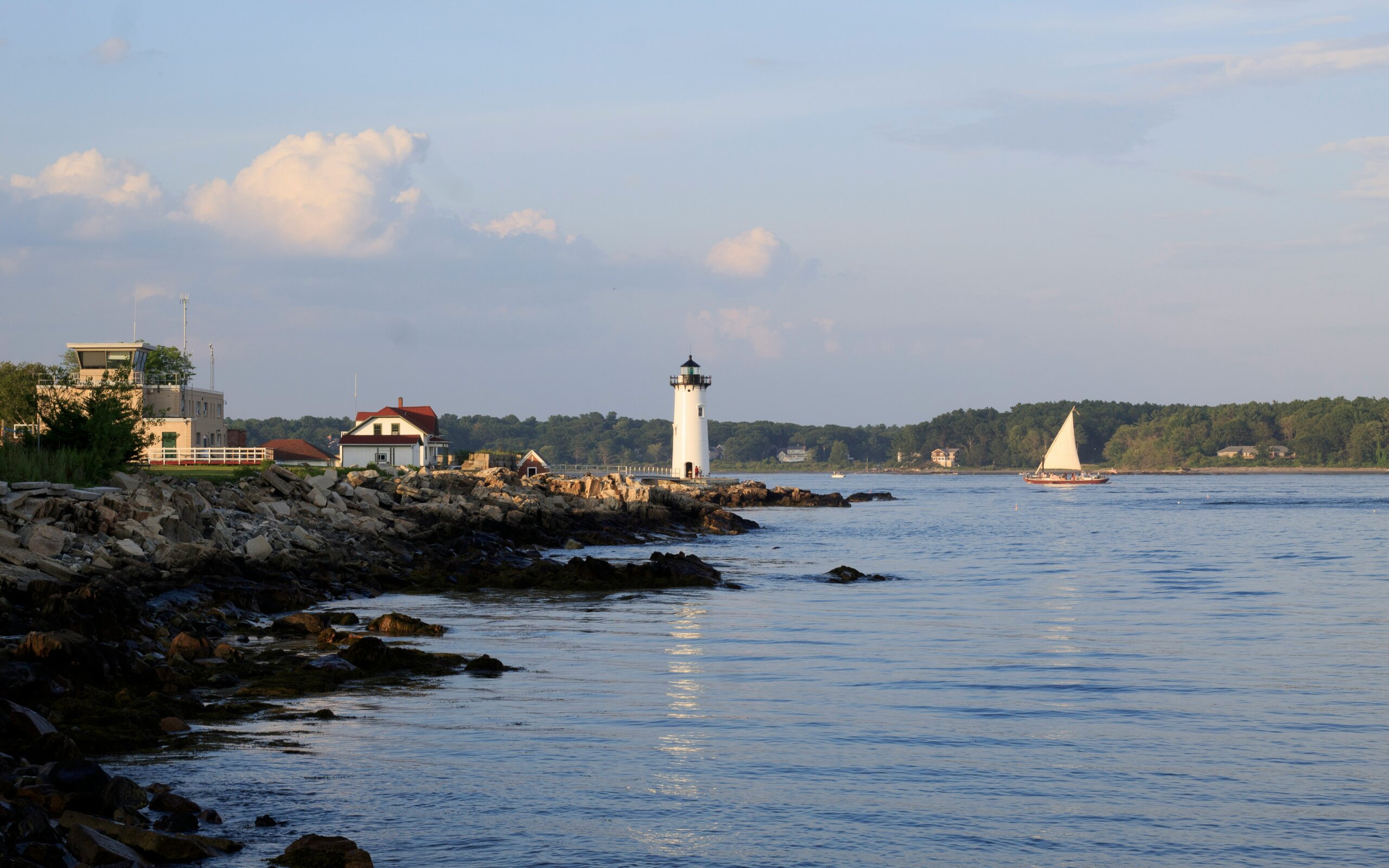 Scenic view of a historic lighthouse in New Castle, New Hampshire, perched on a rocky shoreline with ocean waves and a backdrop of classic New England charm.