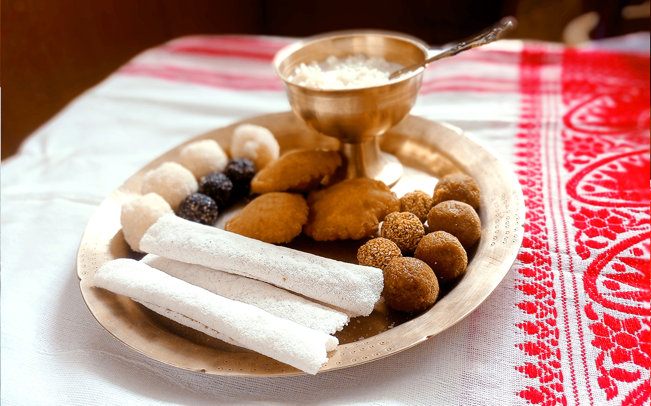 Assamese traditional food items like pitha, laddu, doi sira with assamese gamosa background with japi motifs
