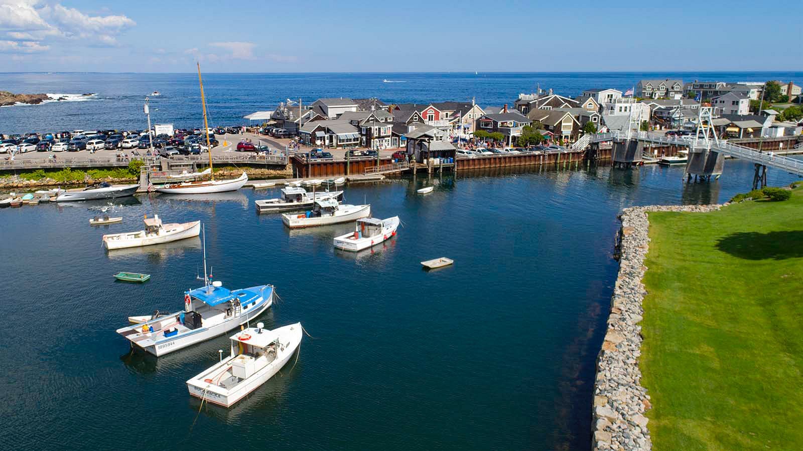 Aerial view of lobster boats and fishing vessels anchored in Perkins Cove harbor in Ogunquit Maine on a sunny summer day with the pedestrian footbridge and shops visible