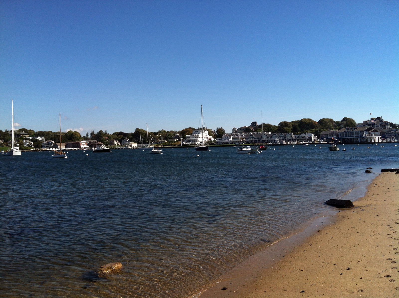 Scenic coastline in Watch Hill, Rhode Island, with rocky shores, upscale homes on distant bluffs, and a peaceful stretch of beach under a soft coastal sky.