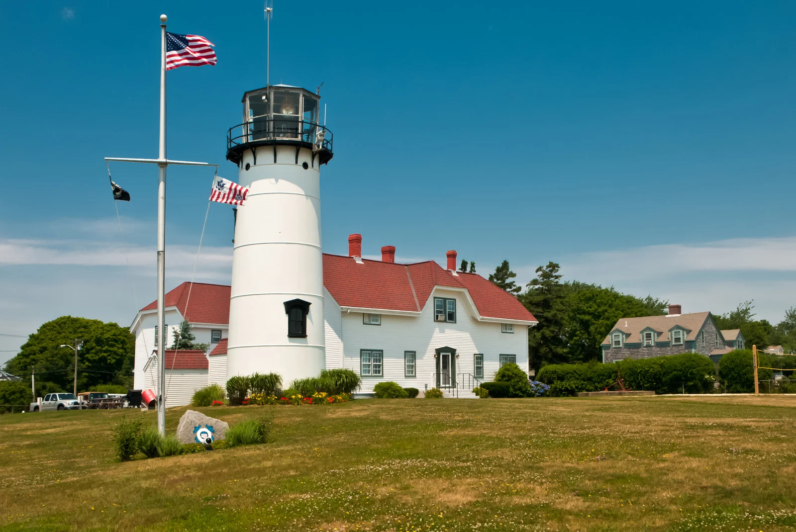 Historic white lighthouse in Chatham, Massachusetts, standing tall on a grassy hill with classic red roof and weathered charm under an open sky.