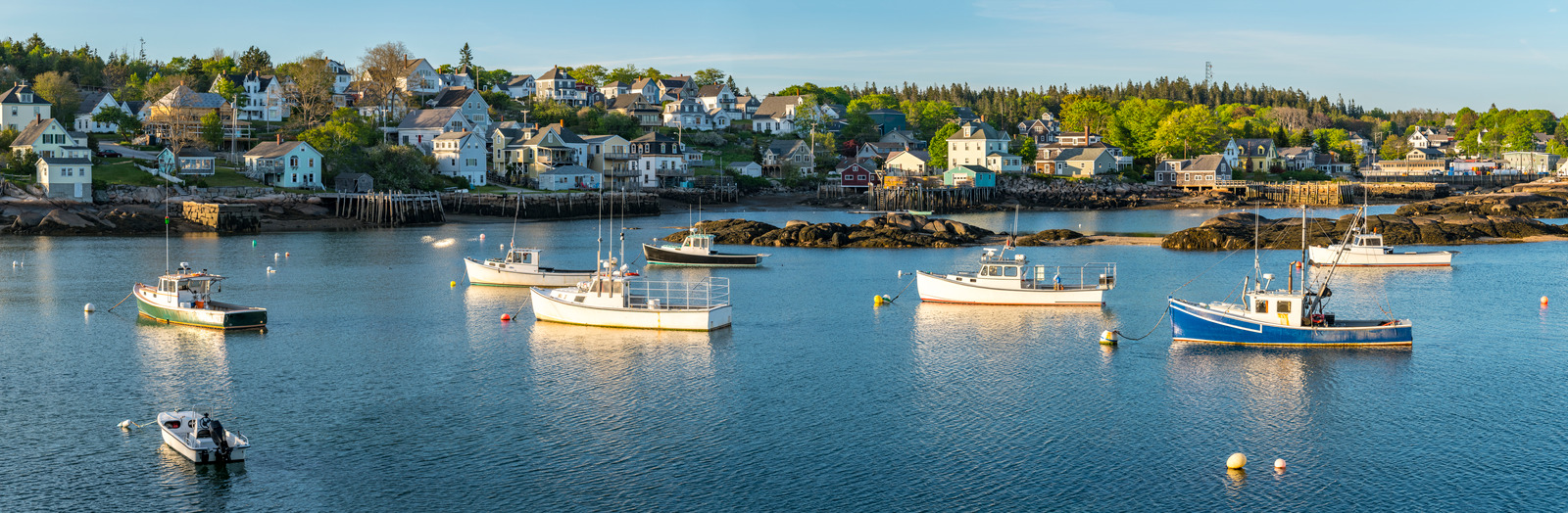 Peaceful harbor scene in Stonington, Maine, with fishing boats, weathered docks, and coastal houses nestled along a rocky shoreline under a soft morning light.
