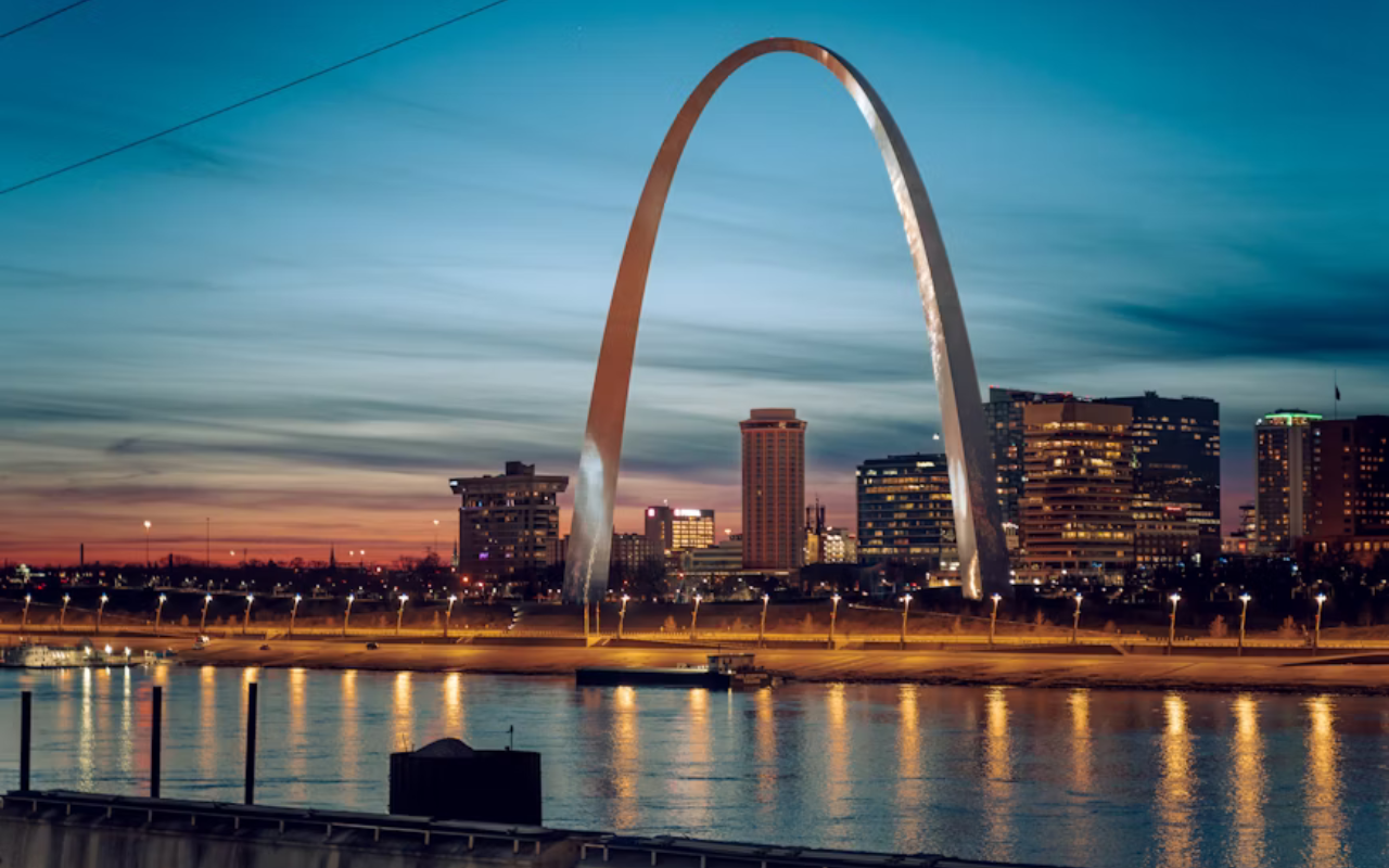 Gateway Arch in St. Louis framed by green park space and blue sky, representing the city’s historical significance.
