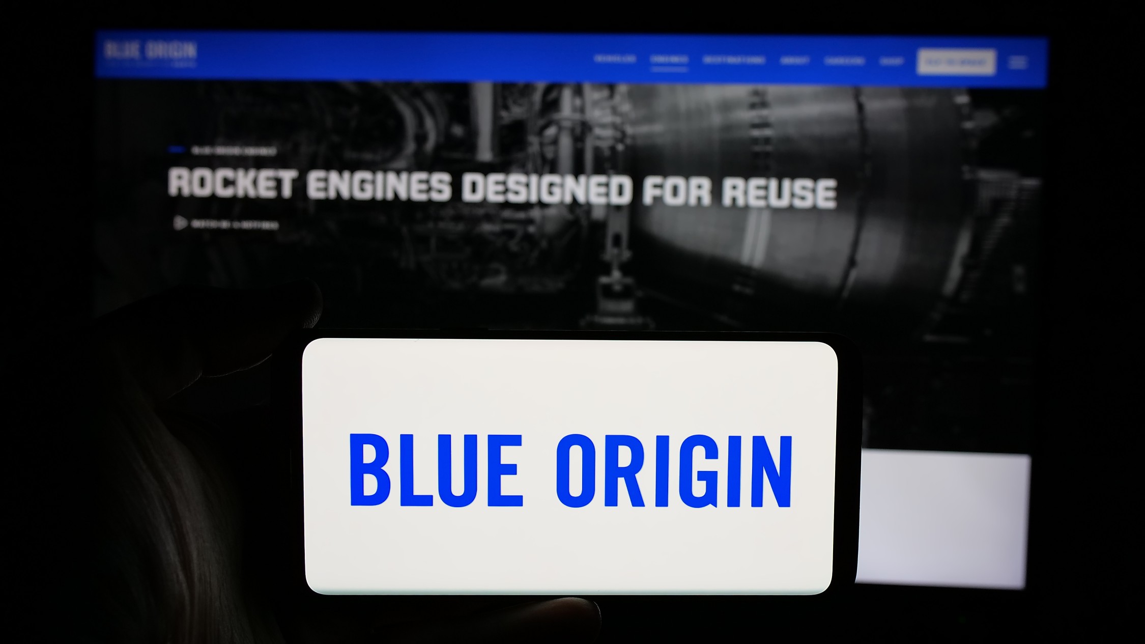 Person holding smartphone displaying Blue Origin logo in front of the company's official website