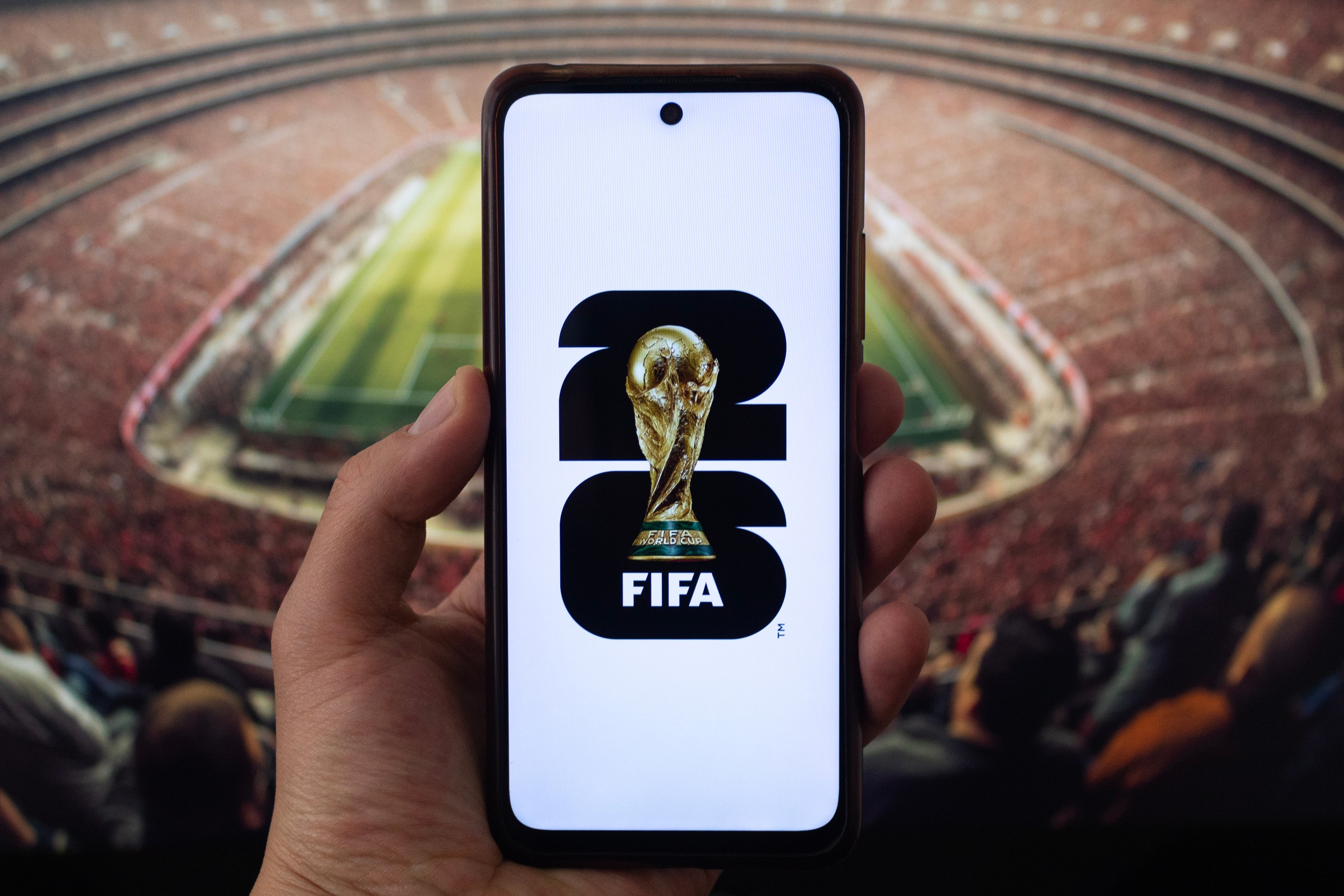 FIFA World Cup 2026 logo on smartphone with stadium background, symbolizing rising international travel and airport demand in the United States.