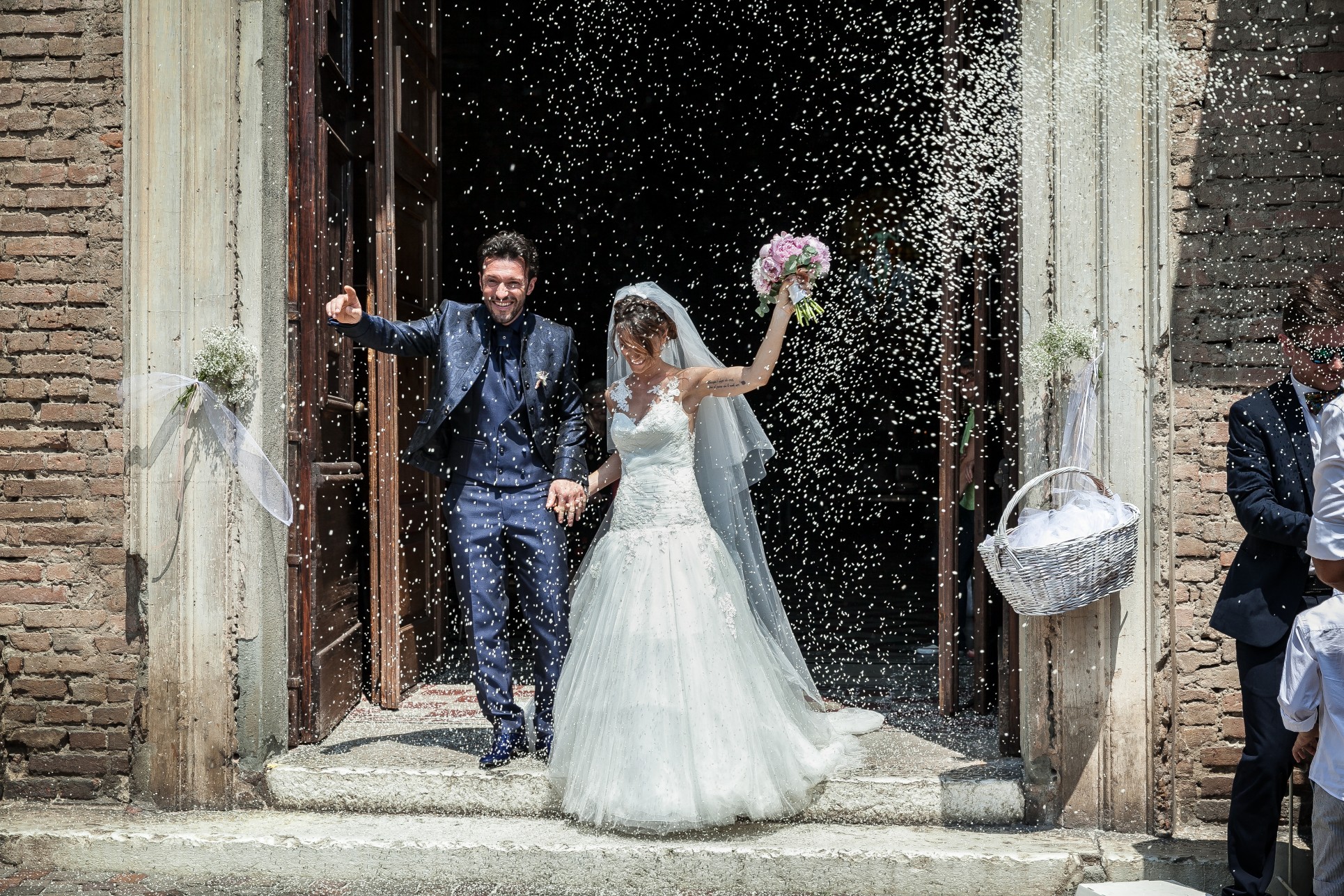 Bride and groom leaving a historic church, smiling as guests throw rice in celebration.