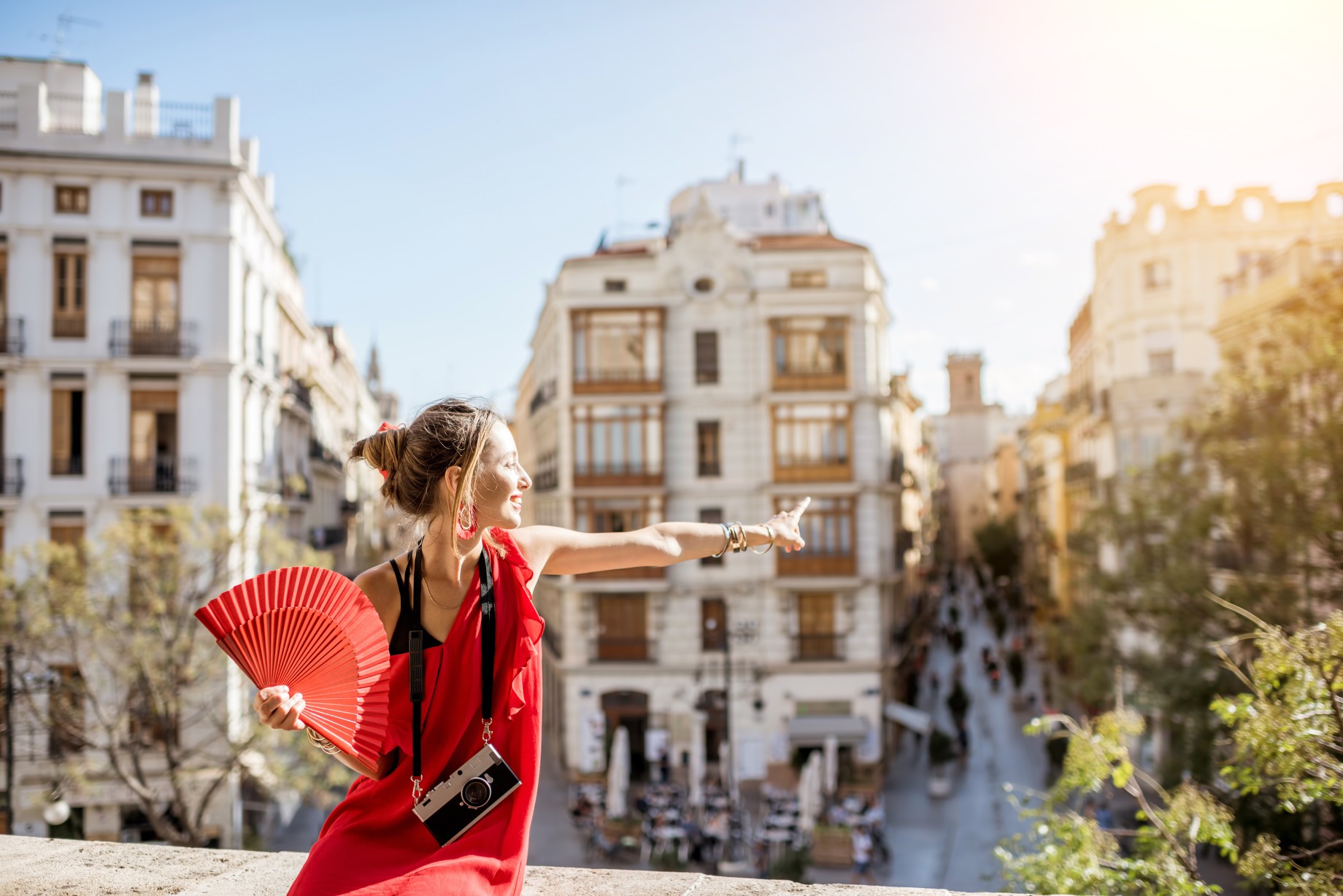 Young woman in red dress with hand fan and photo camera enjoying beautiful cityscape view on Valencia city during the sunny weather in Spain