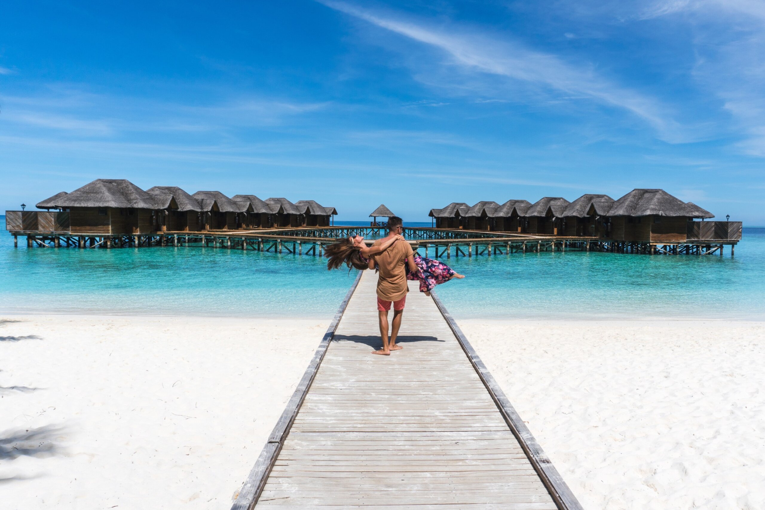 Man holding wife on honeymoon in Maldives on overwater bungalow bridge with ocean beach view – luxury tropical honeymoon destination 2025