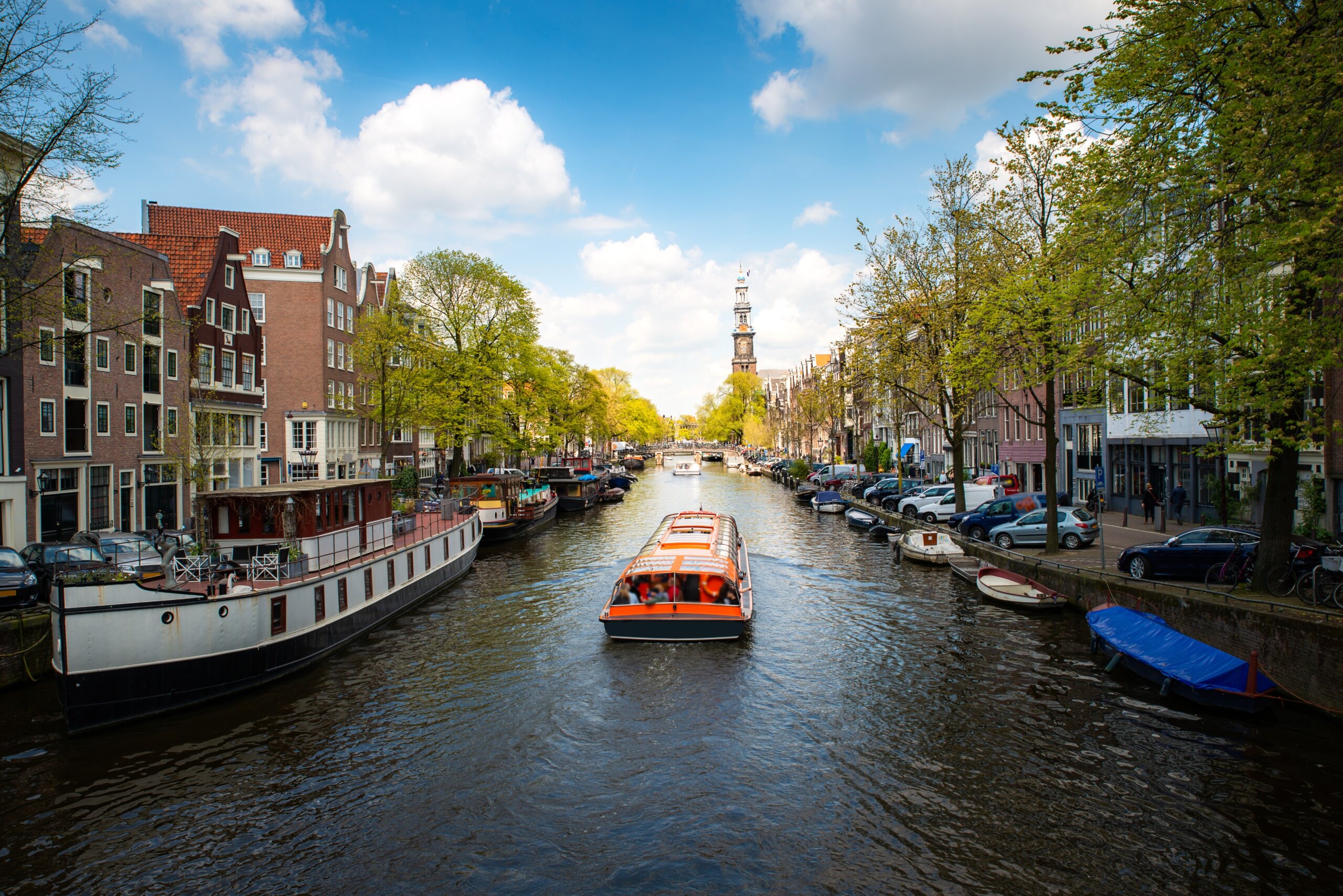 Amsterdam canal with a cruise boat passing traditional Dutch houses, showcasing the historic architecture and culture of the Netherlands