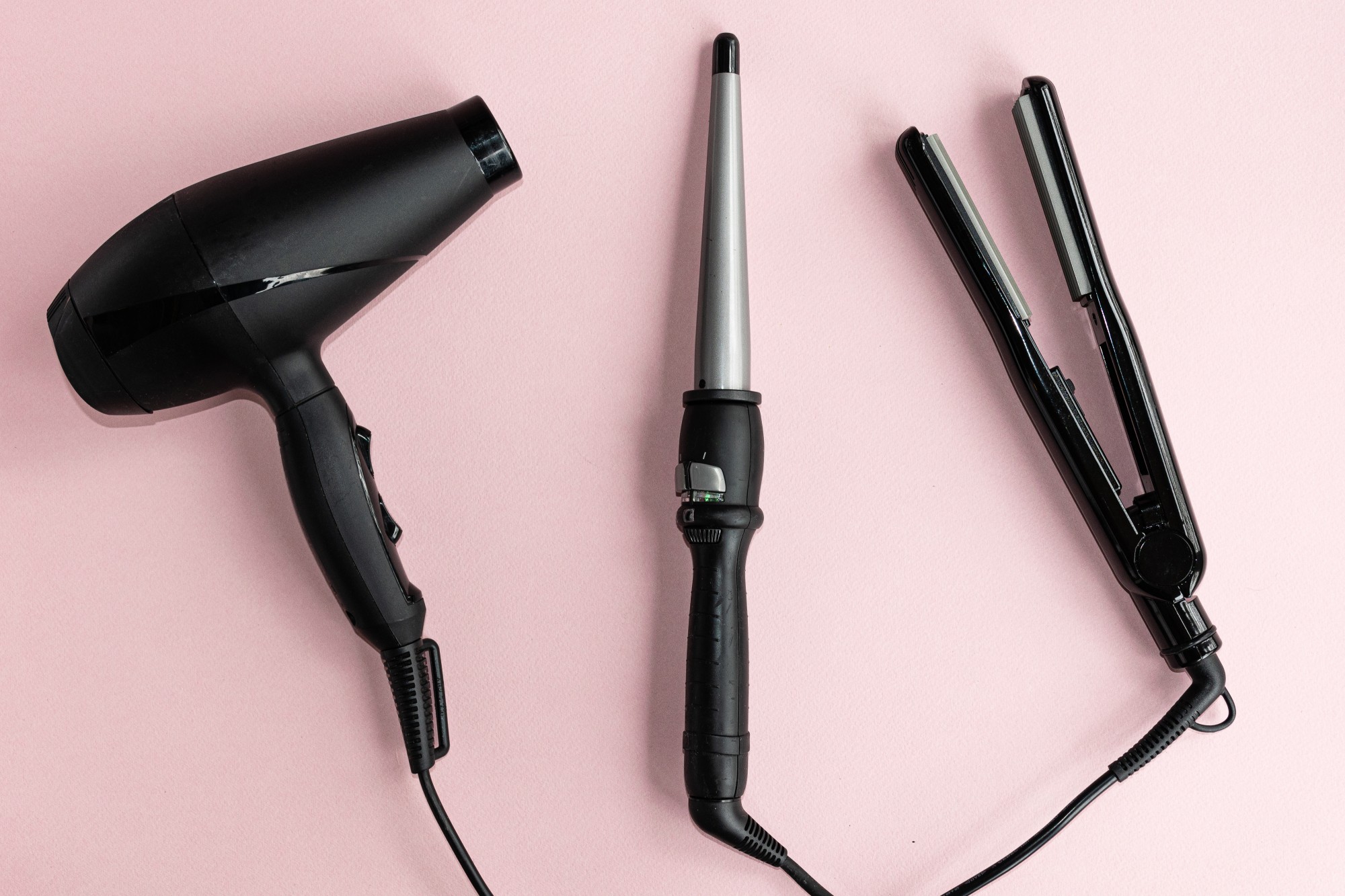 Black hair dryer, curling iron and hair iron on a pink background. .Professional hairdresser set. Tools necessary for hair care.