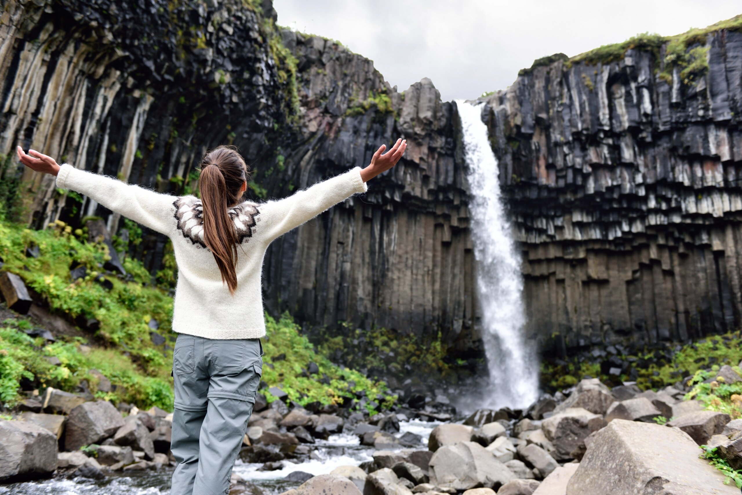 Woman admiring Svartifoss waterfall in Skaftafell, Iceland, a famous natural landmark and popular tourist attraction.