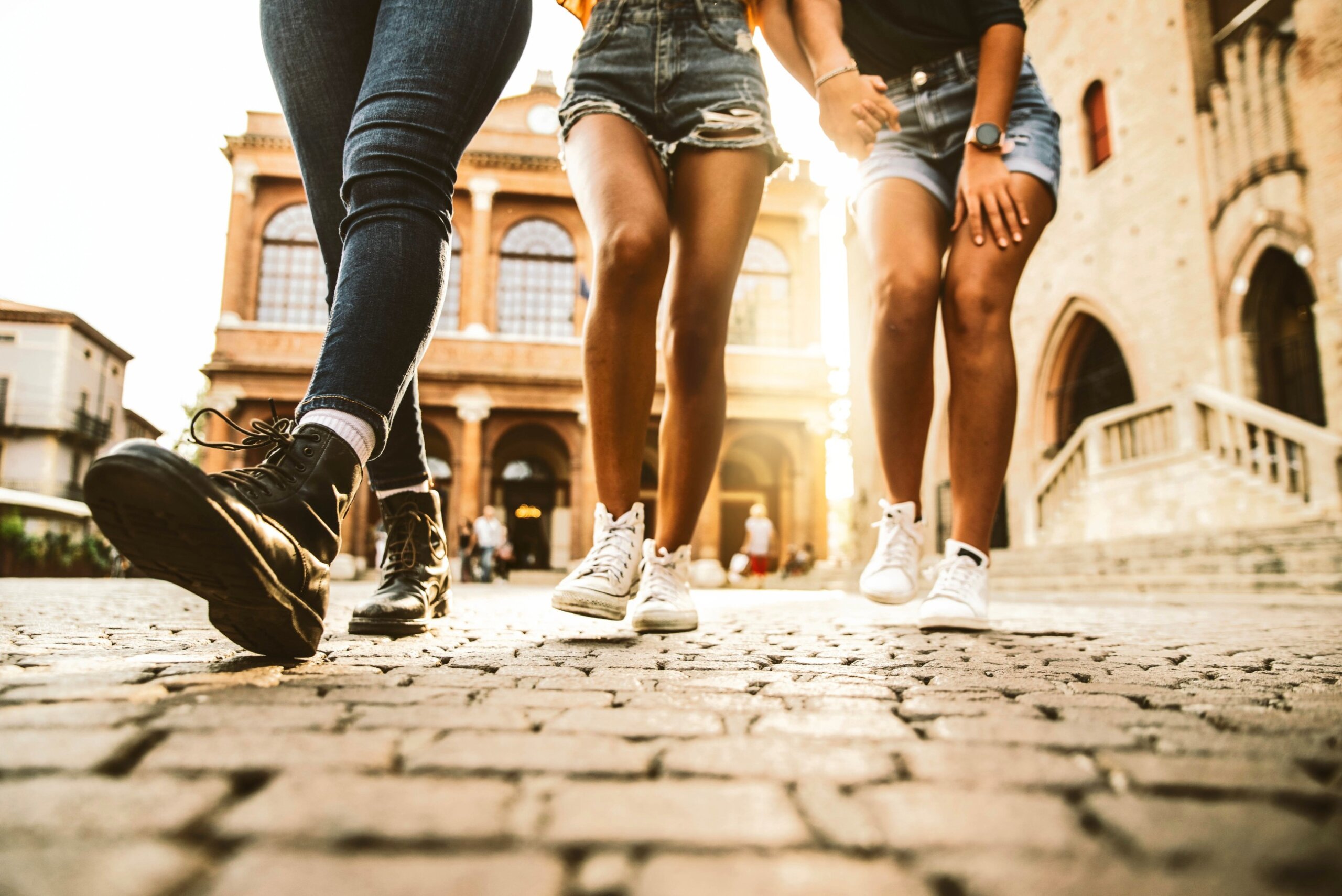 Female friends walking outdoors at sunset - Group of tourists having fun together on city street with backlight - Leg view - Tourism, females, happy lifestyle concept