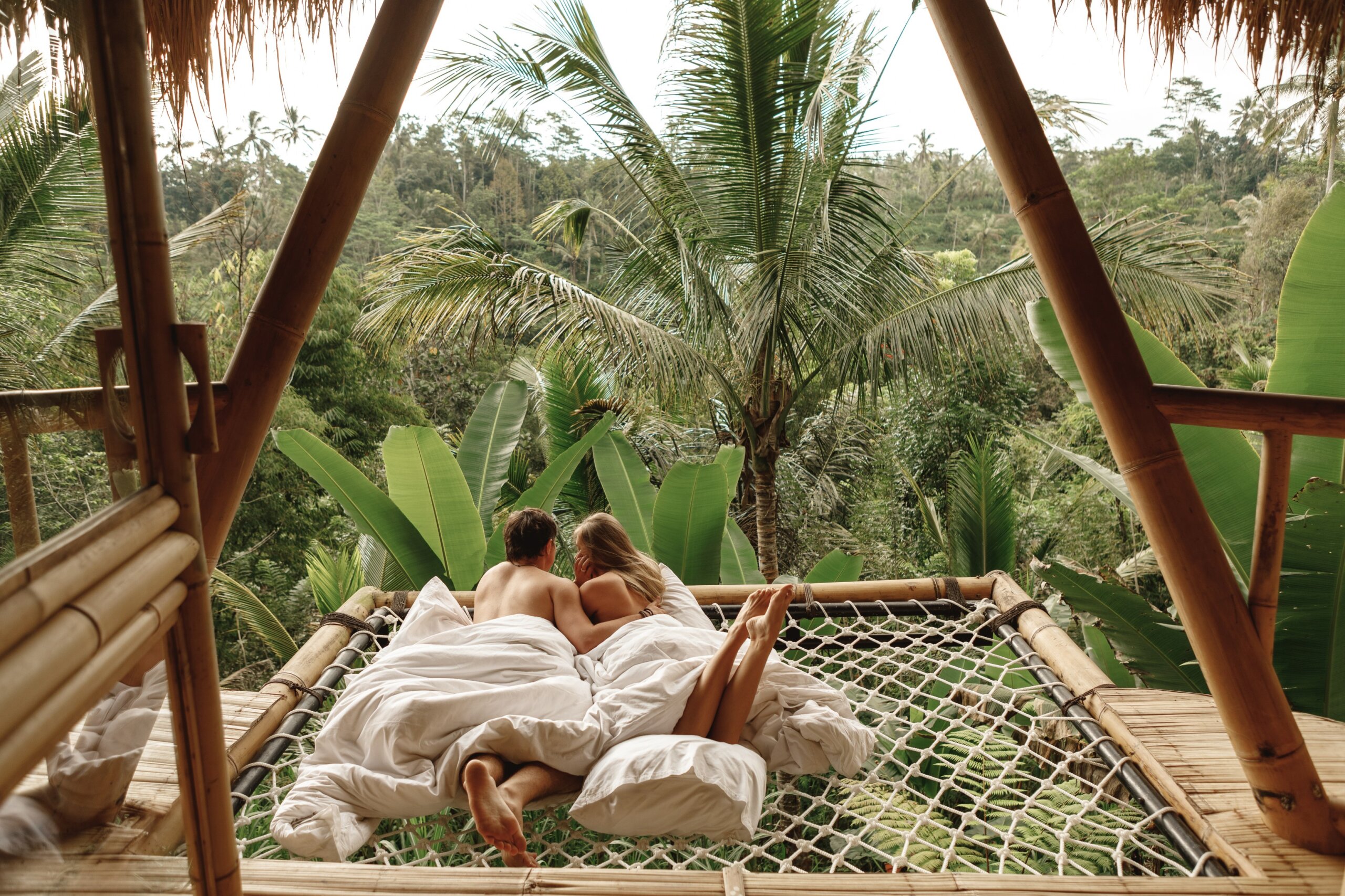 Couple on honeymoon in Bali relaxing in jungle tree house hammock – romantic Bali honeymoon destination 2025