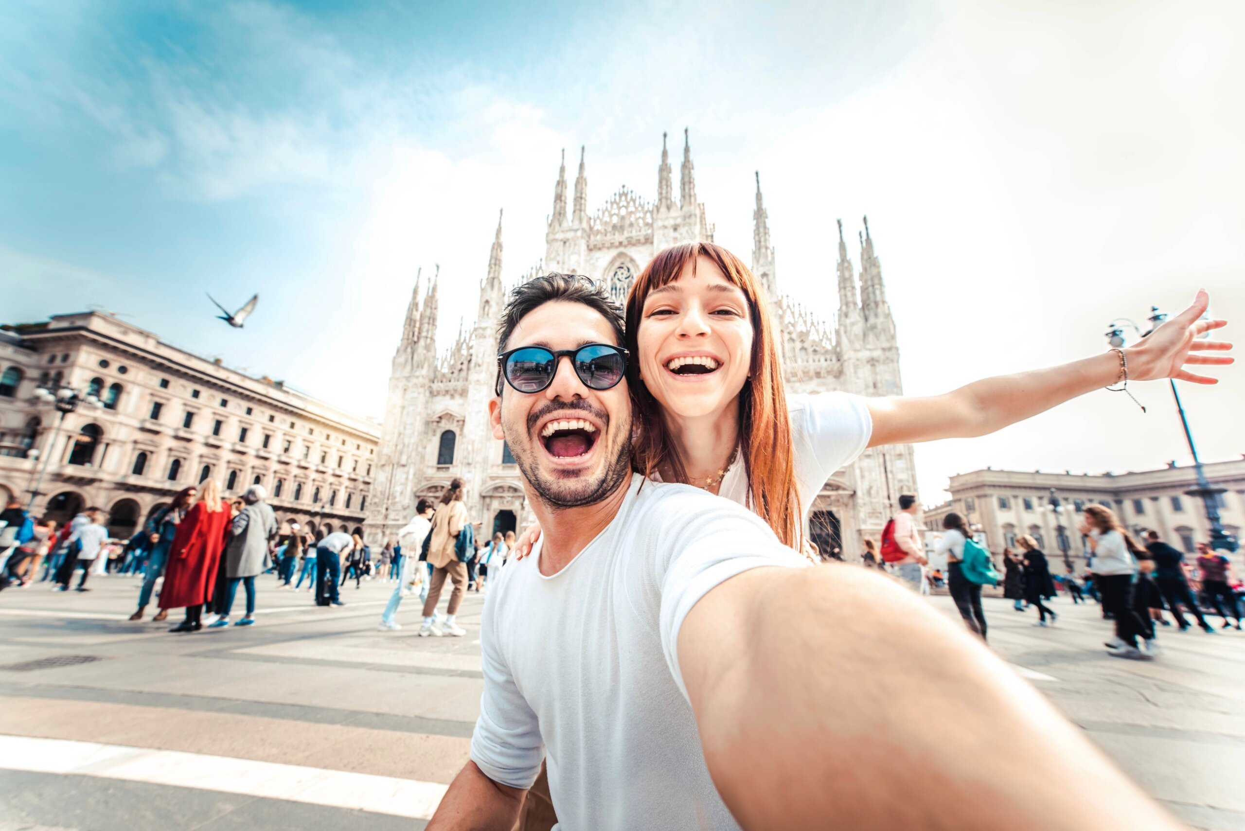 Happy couple taking selfie in front of Duomo cathedral in Milan, Lombardia - Two tourists having fun on romantic summer vacation in Italy - Holidays and traveling lifestyle concept