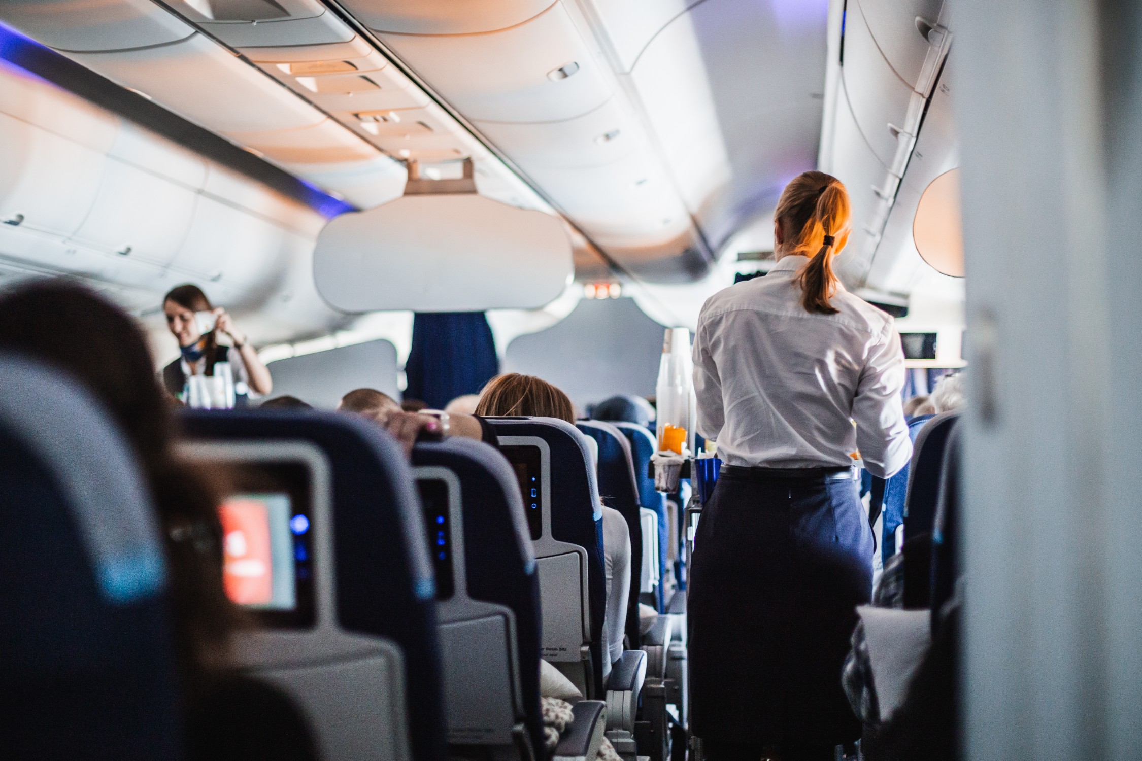 Flight attendants pushing a drink cart down the aisle of a crowded airplane.