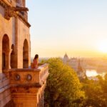 Woman enjoying sunrise view over Budapest from Fisherman’s Bastion with Parliament Building and Danube River in the background.