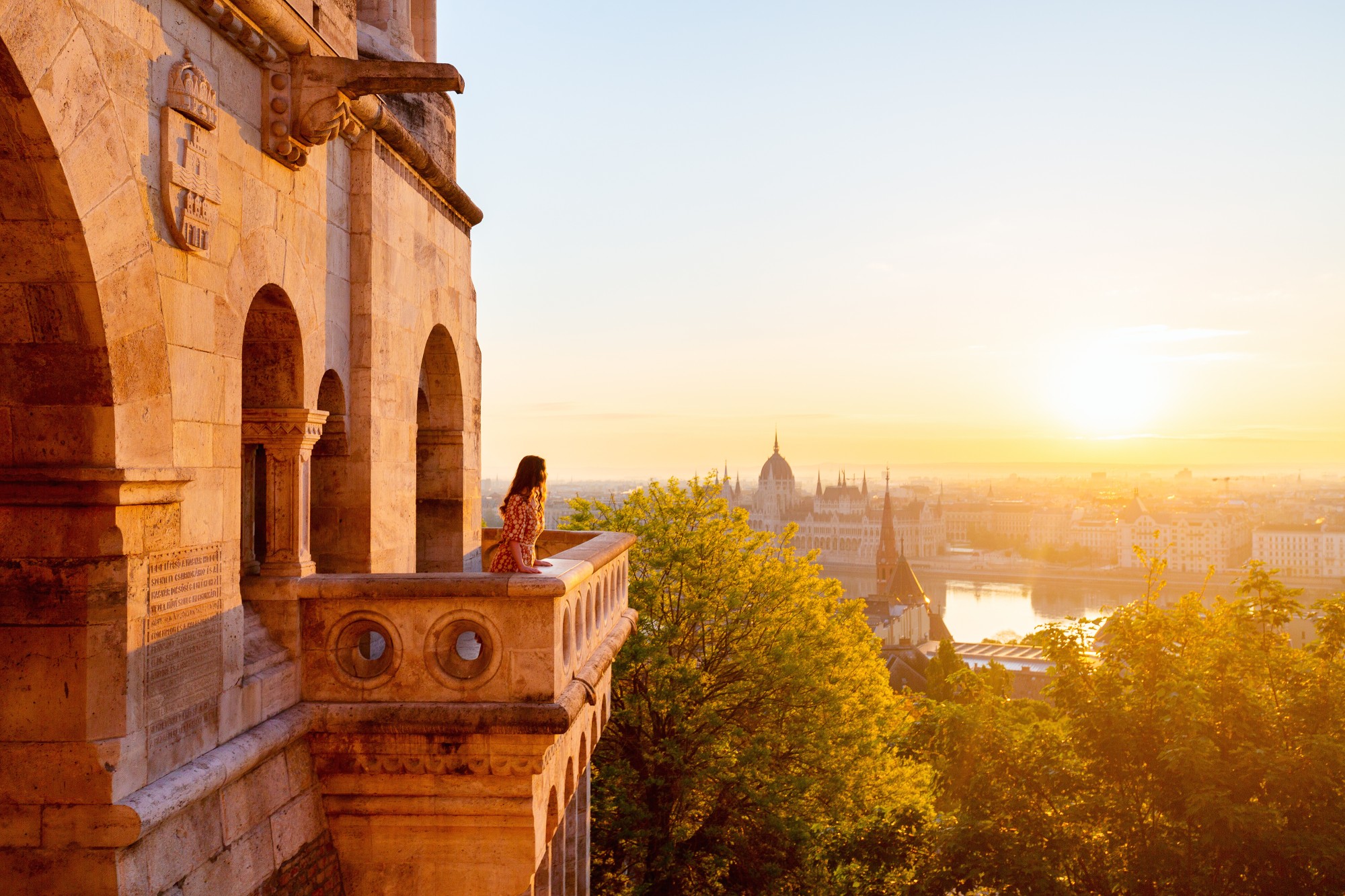 Woman enjoying sunrise view over Budapest from Fisherman’s Bastion with Parliament Building and Danube River in the background.