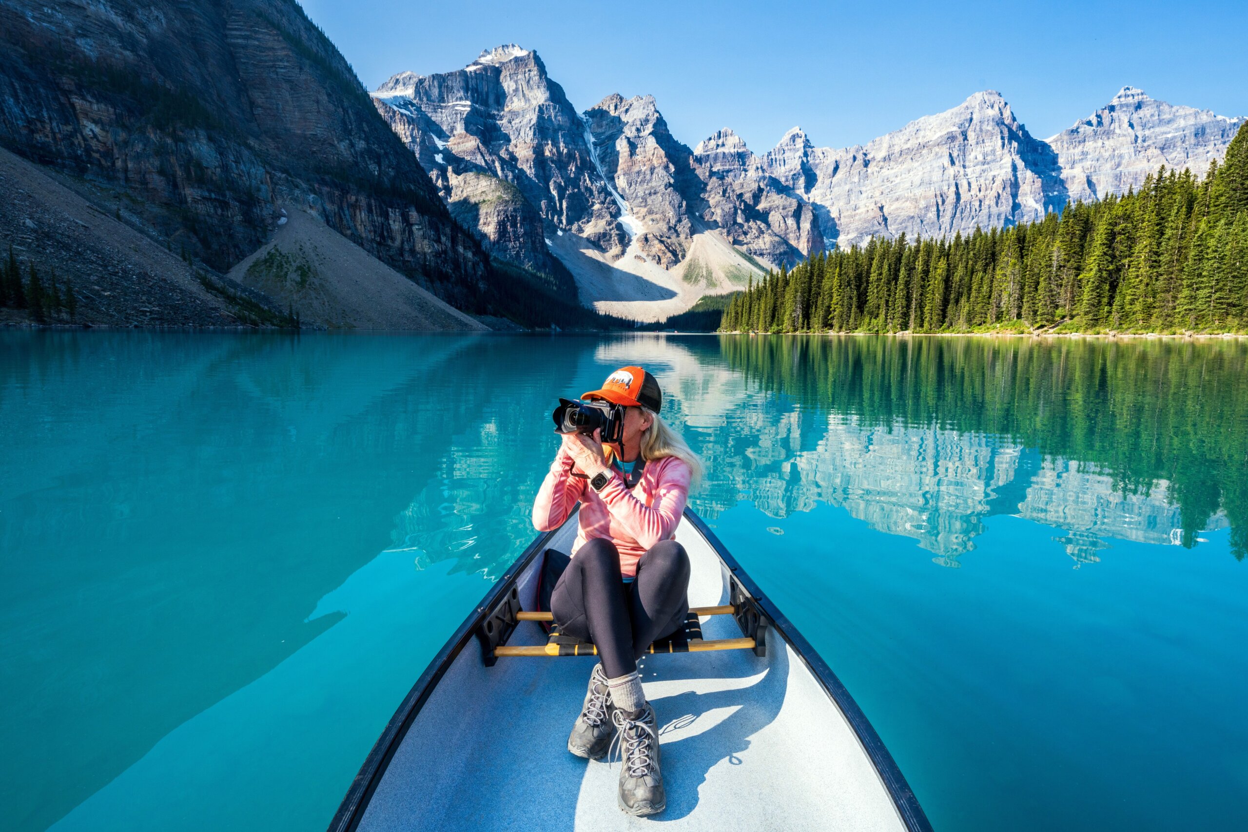 Woman taking Photos of surrounding Mountains, on Moraine Lake during summer in Banff National Park, Canadian Rockies, Alberta, Canada.