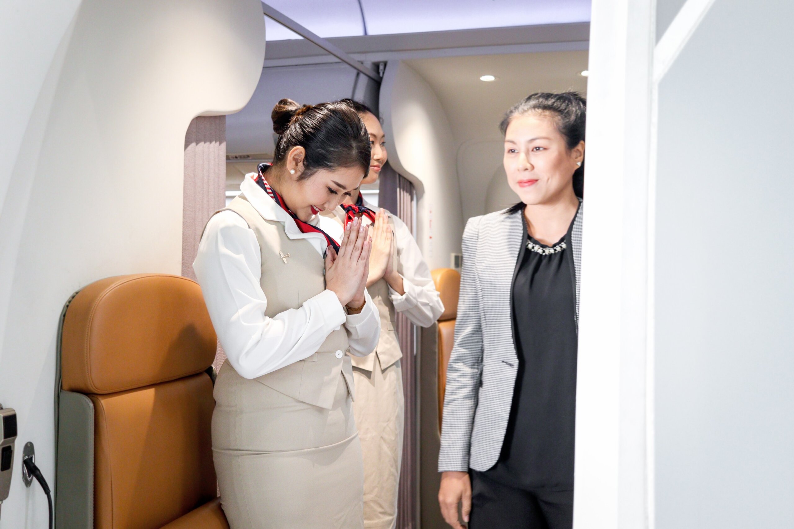 Beautiful Asian female air hostess standing and greeting at airplane entrance gate after plane landing, flight attendant say goodbye to passenger, cabin crew work in airplane, Airline transportation.