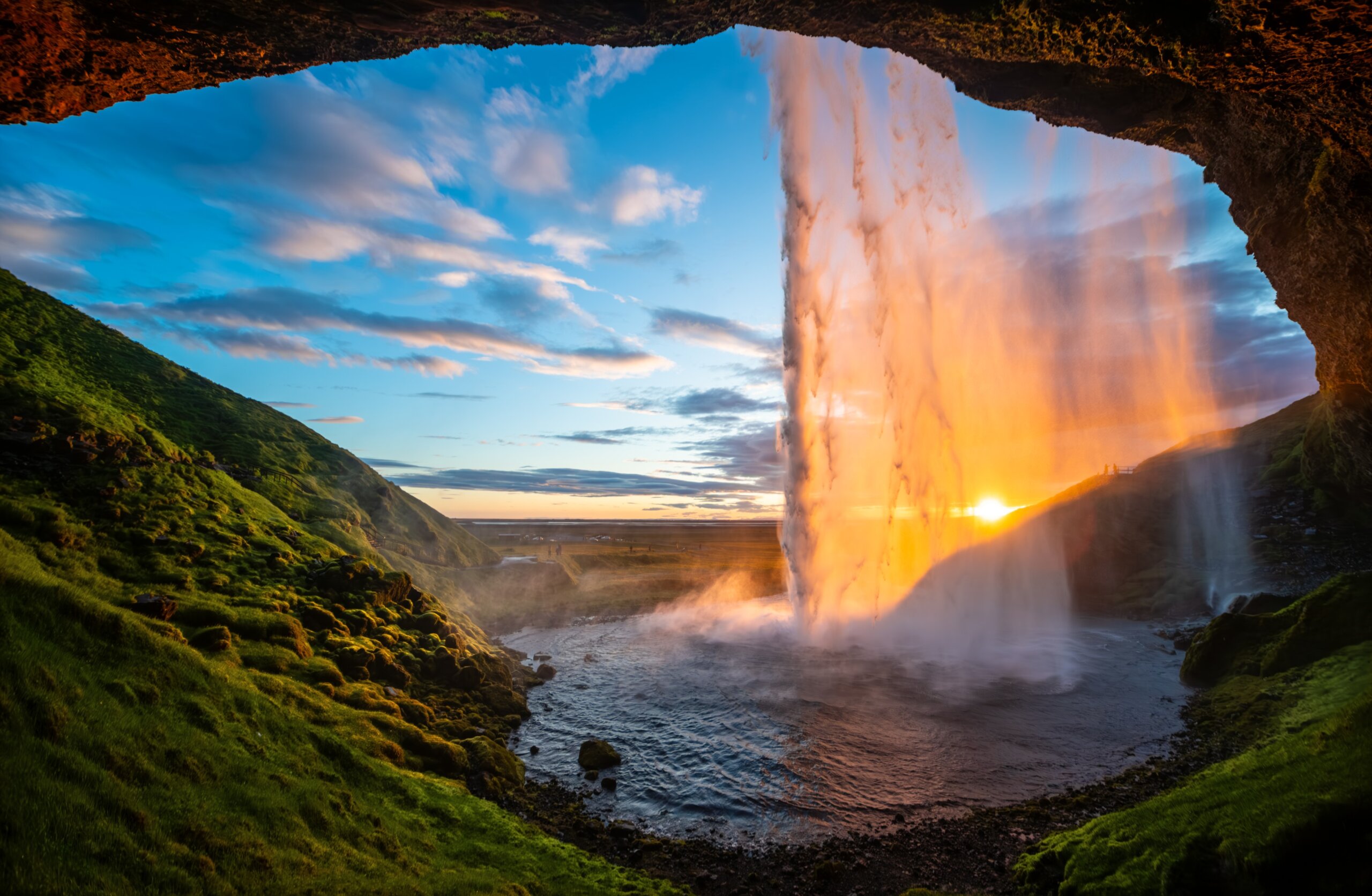 Impressive waterfall “Seljalandsfoss“ in Iceland seen from a cave behind the sunlit water curtain at midnight in June. 