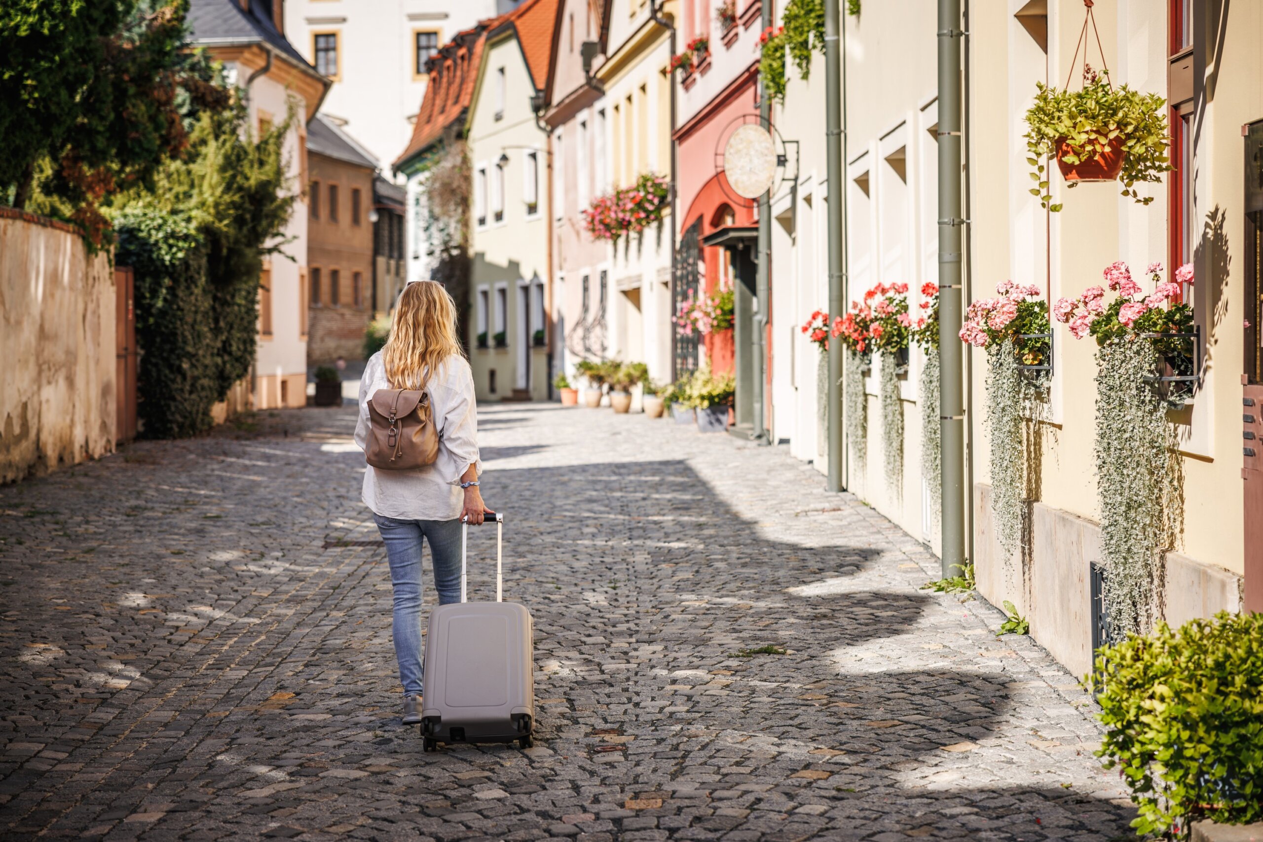Solo travel. Woman tourist with suitcase and backpack walking on street. Traveling and vacation in european city Olomouc, Czech Republic