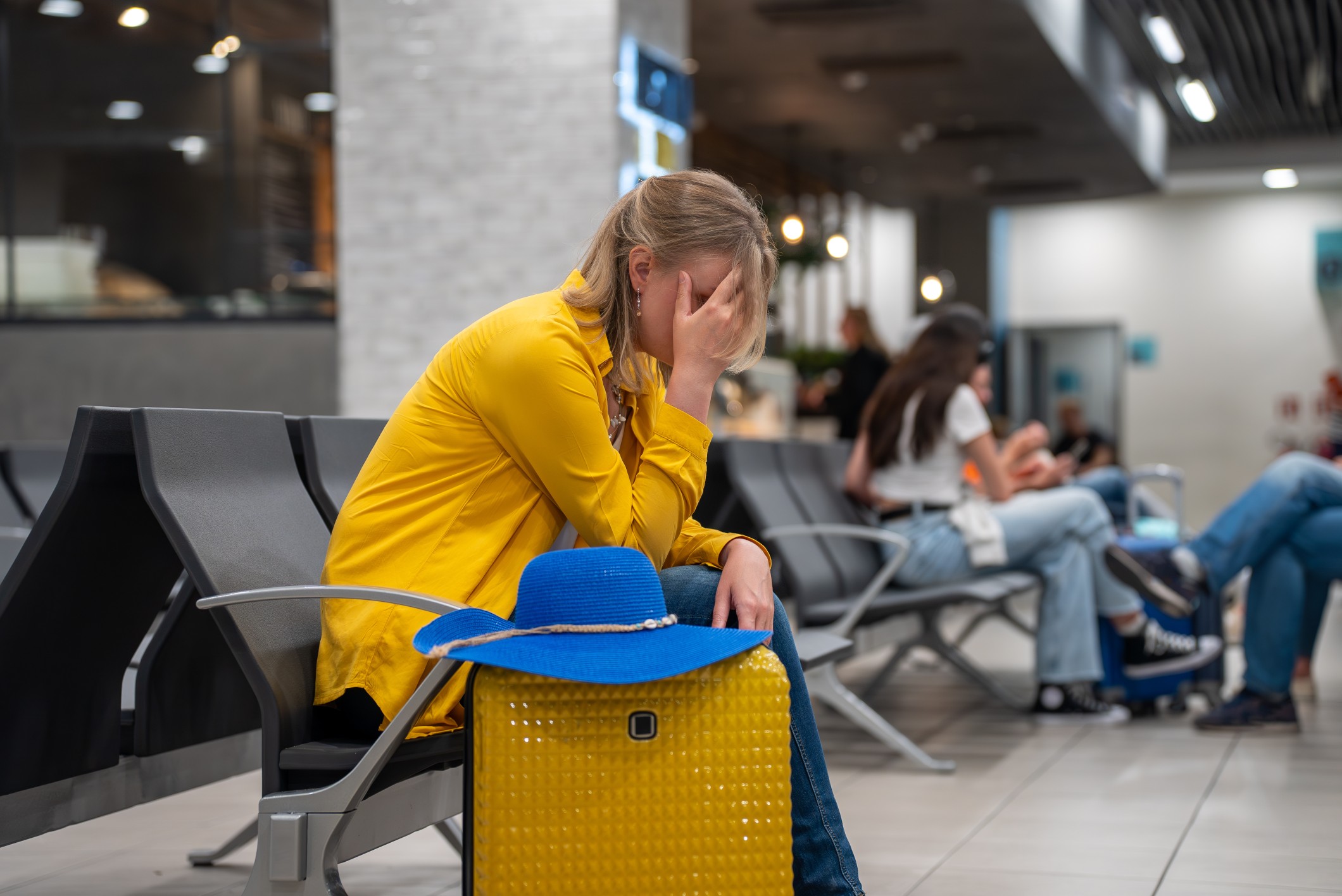 Frustrated woman at airport with suitcase after canceled flight, representing nonrefundable travel struggles.